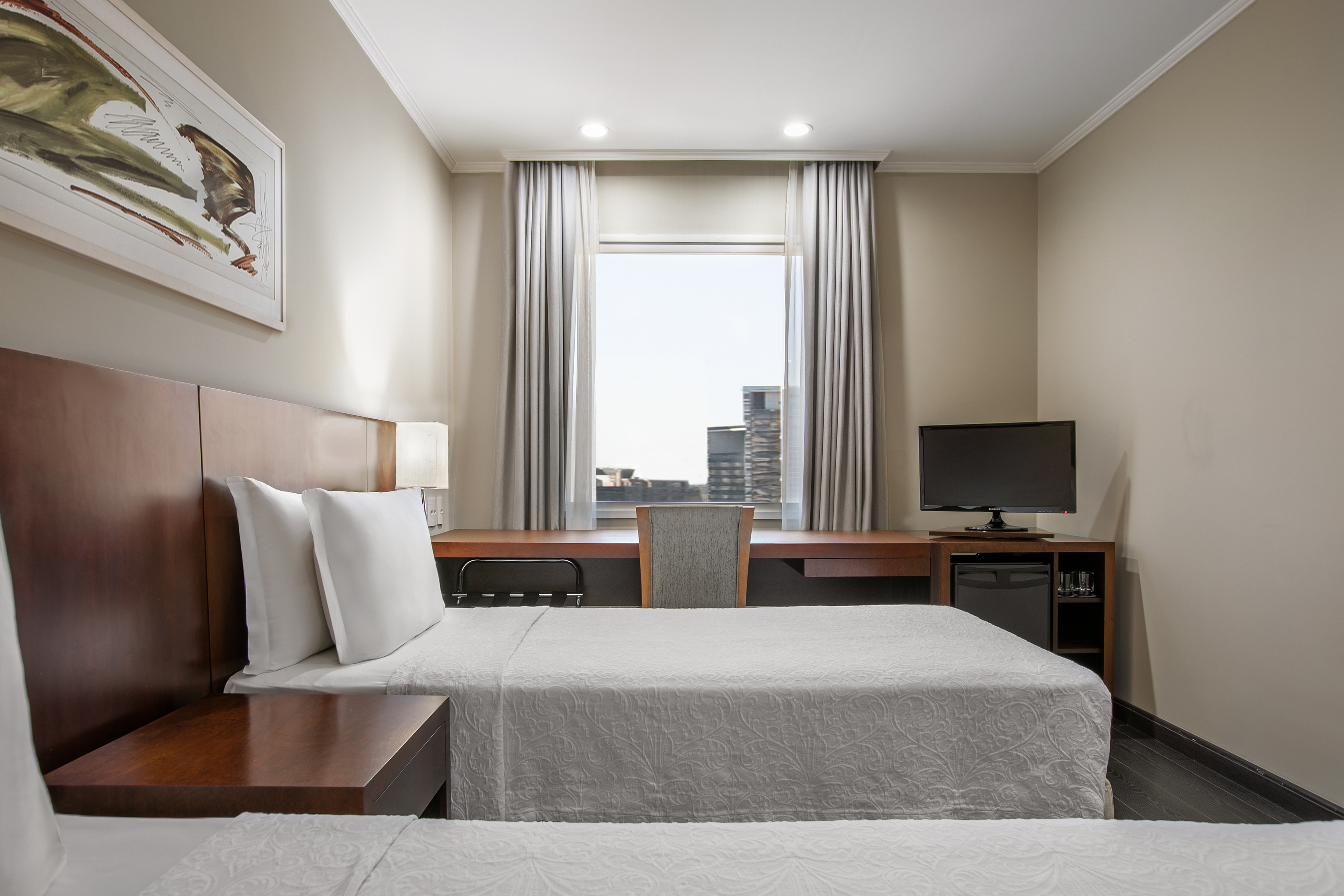 Hotel room with two twin beds, city view, desk, TV, and mini-fridge.
