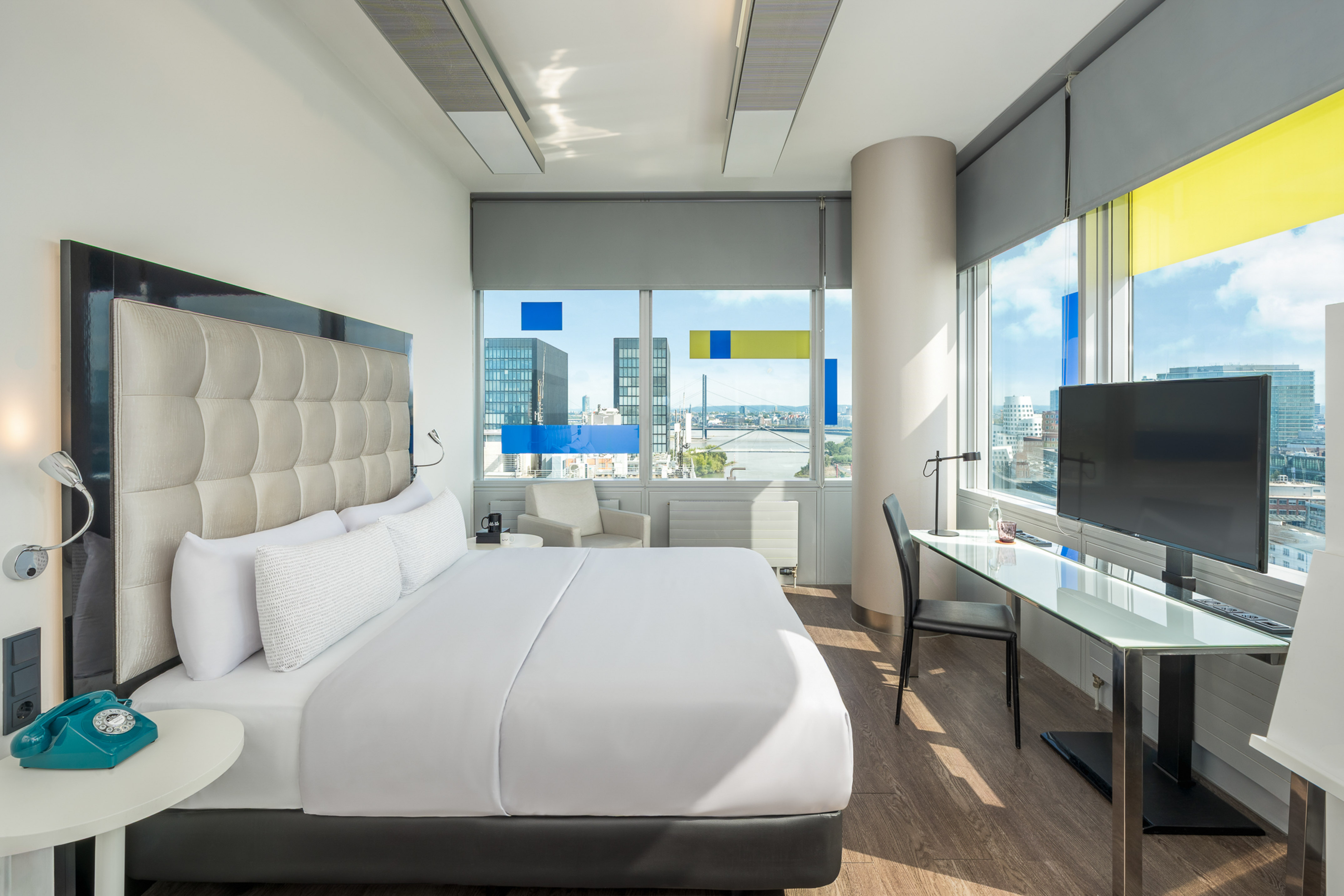Modern hotel room with city and waterfront view, large bed, and work desk.