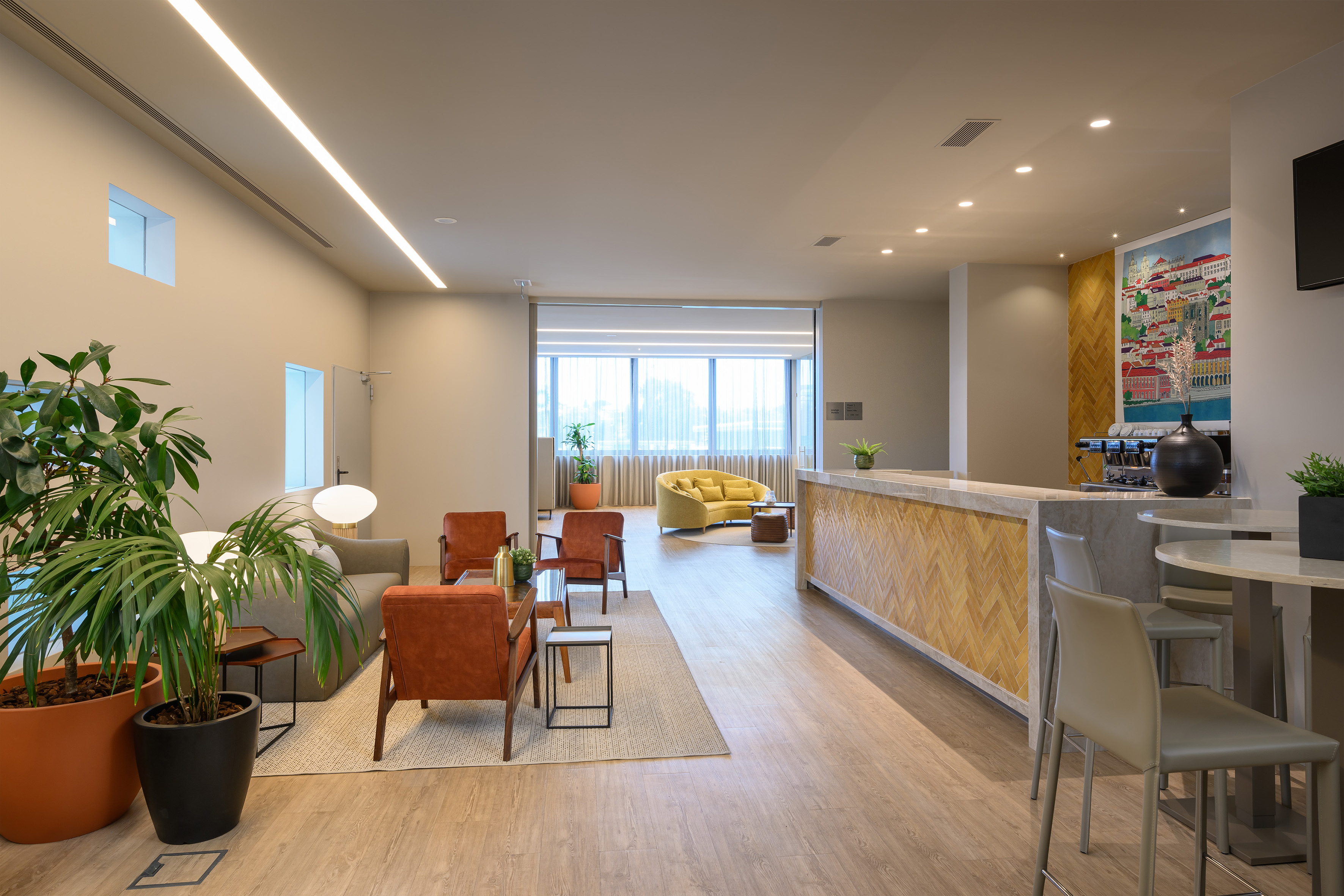 Modern lounge area with comfortable seating, green plants, and a reception bar.