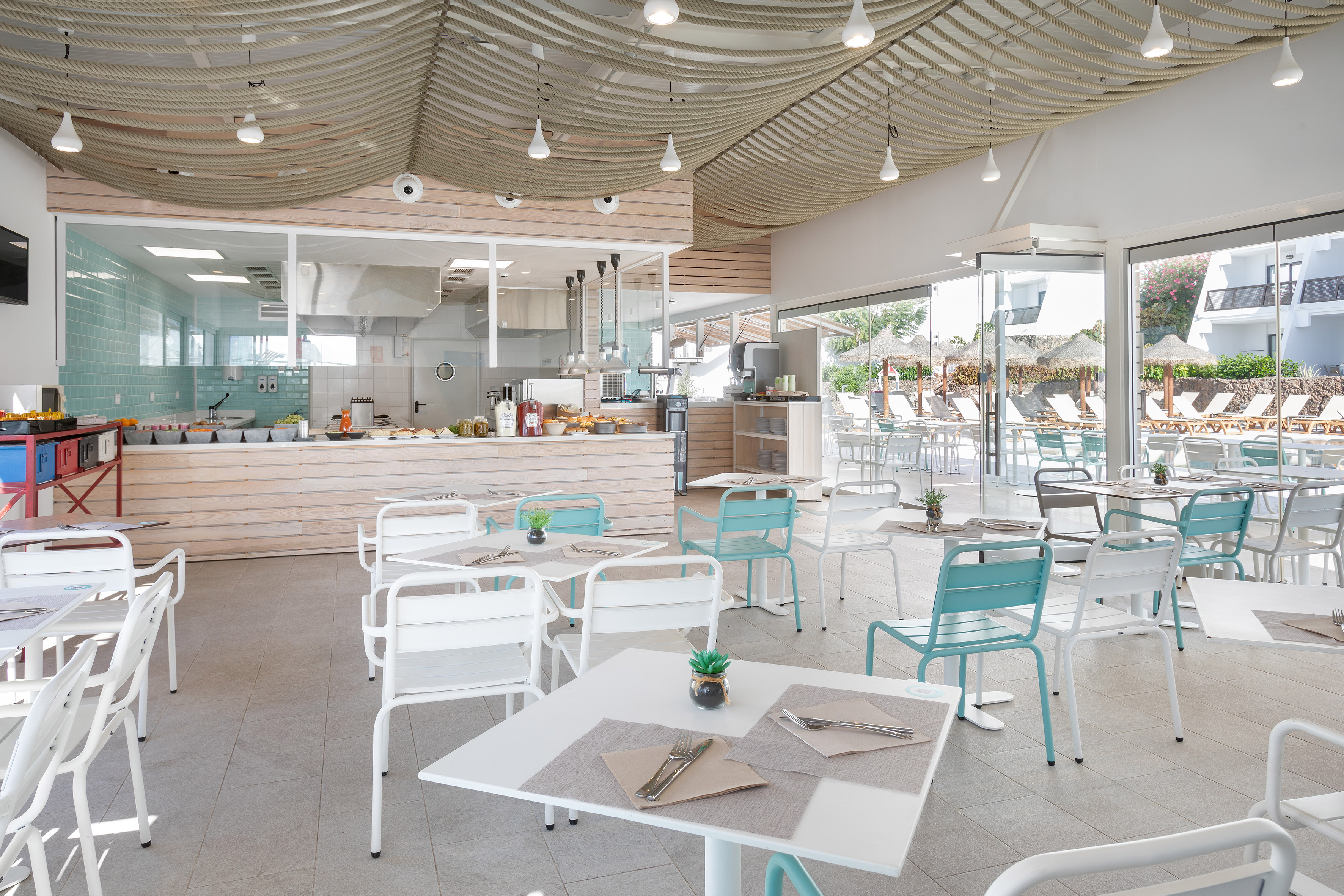 Modern hotel restaurant buffet with rope ceiling, open kitchen, and poolside view.