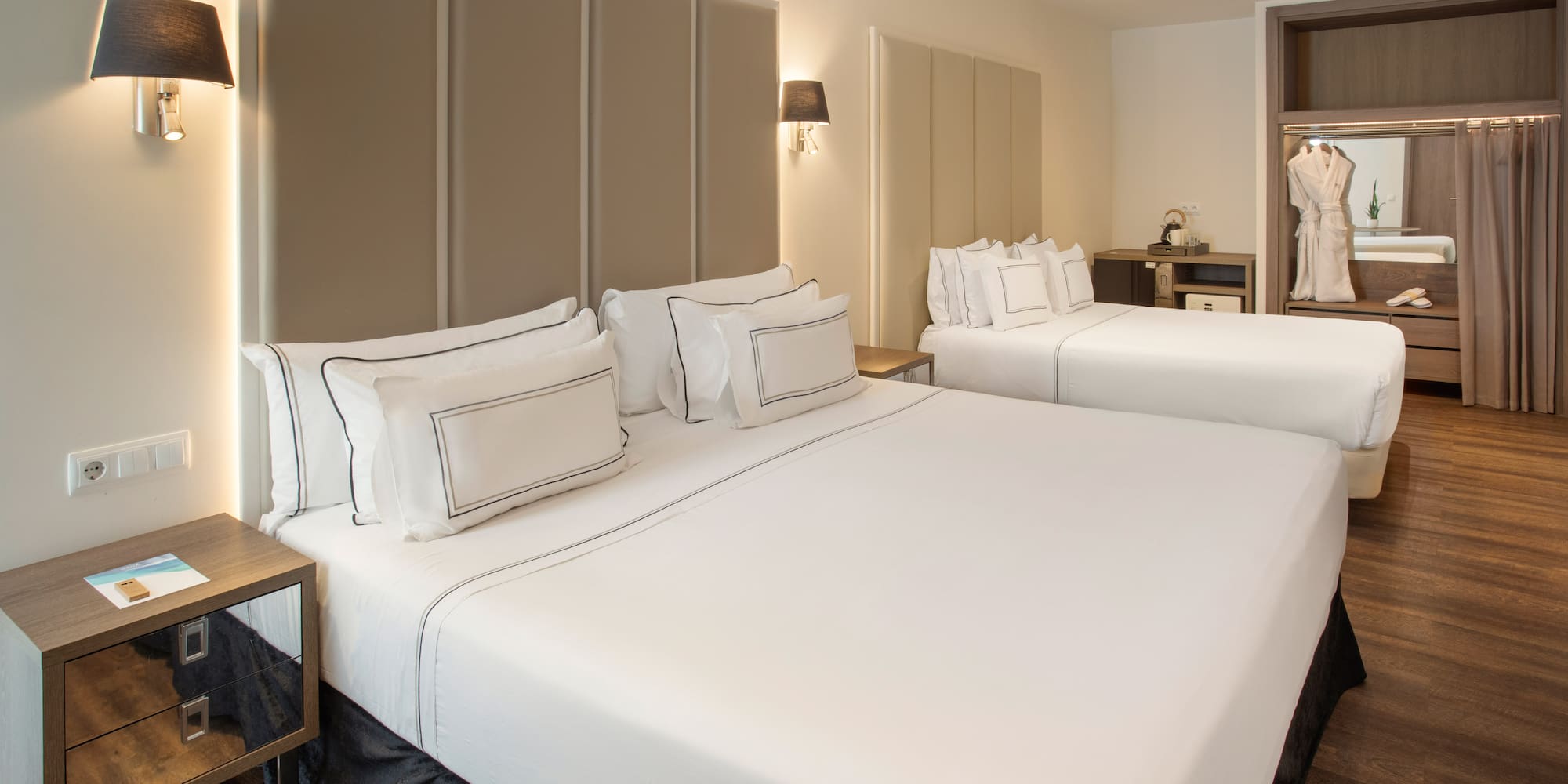 Modern hotel room with two beds, white bedding, upholstered headboards, and a wardrobe.
