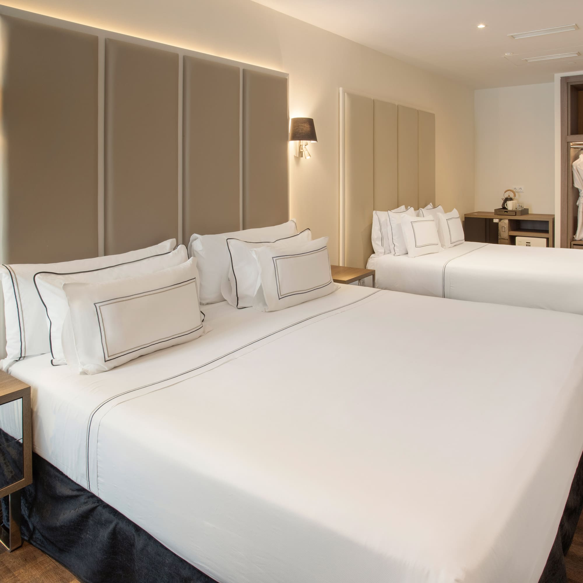 Modern hotel room with two beds, white bedding, upholstered headboards, and a wardrobe.