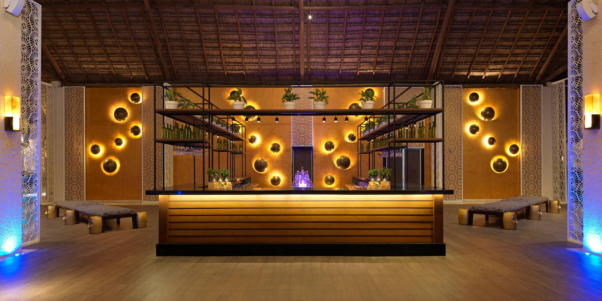 Luxury resort bar with thatched roof, glowing circular wall lights, and modern decor.