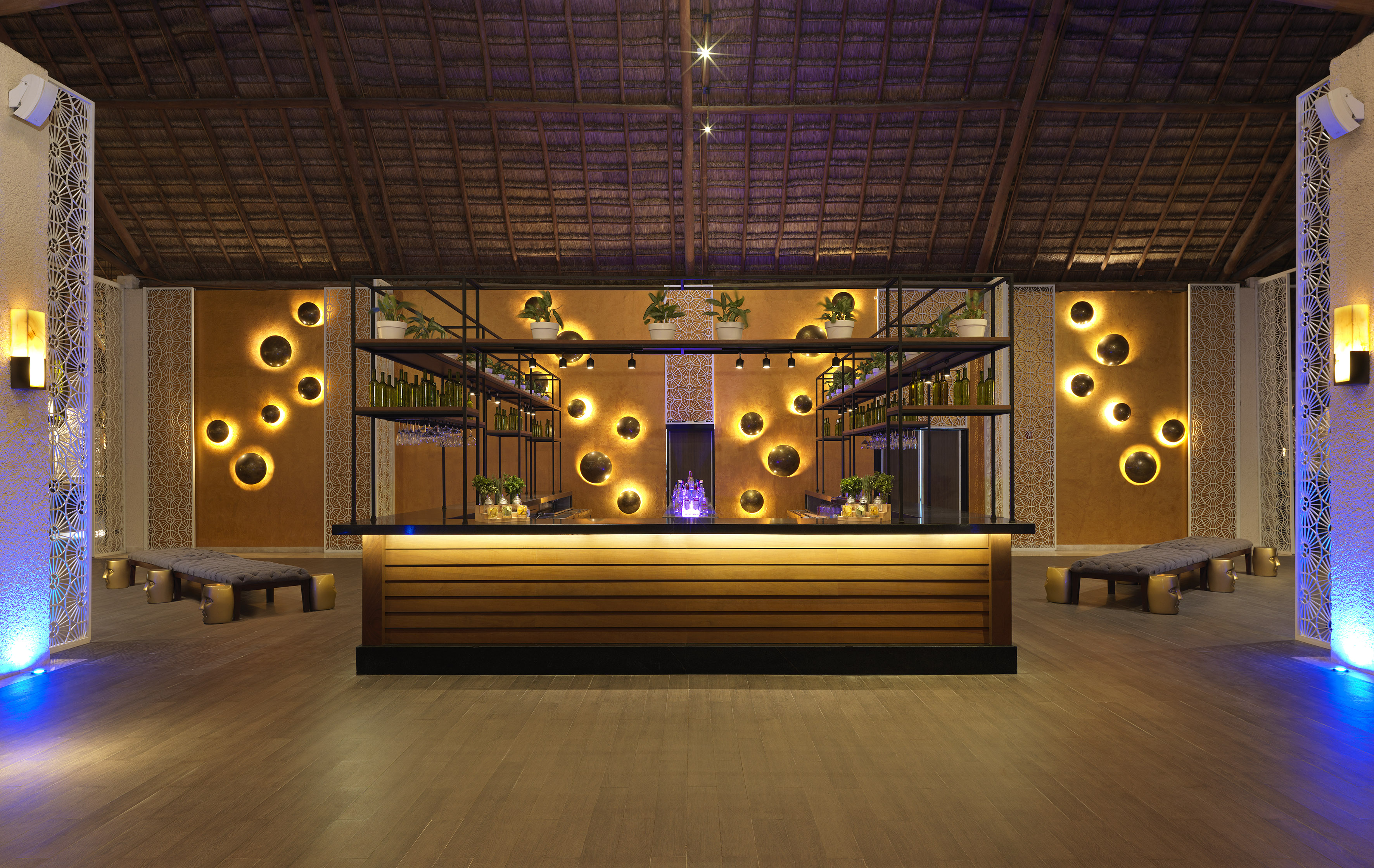 Luxury resort bar with thatched roof, glowing circular wall lights, and modern decor.
