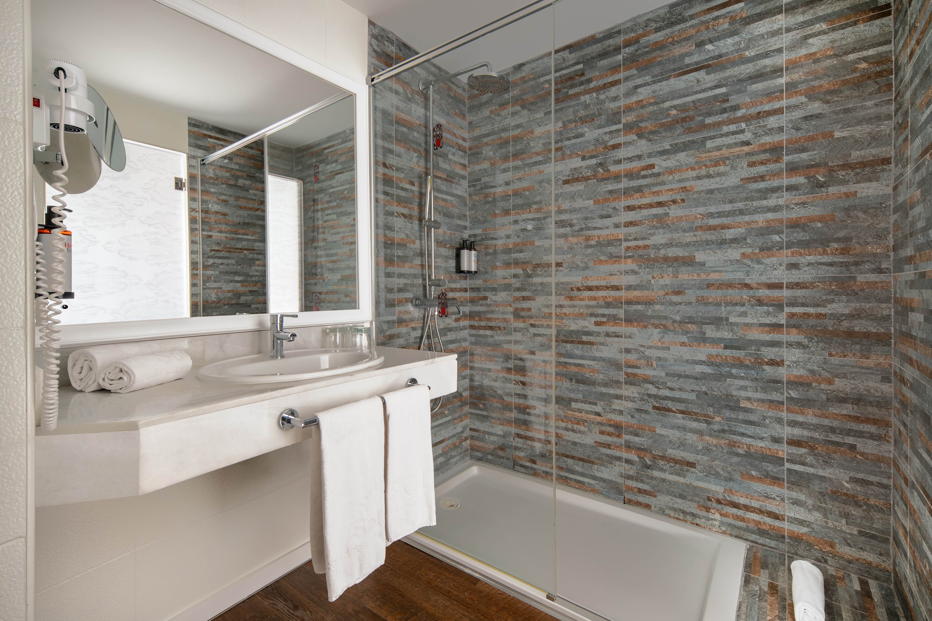 Modern bathroom with white vanity, sink, and shower featuring grey/brown tile.