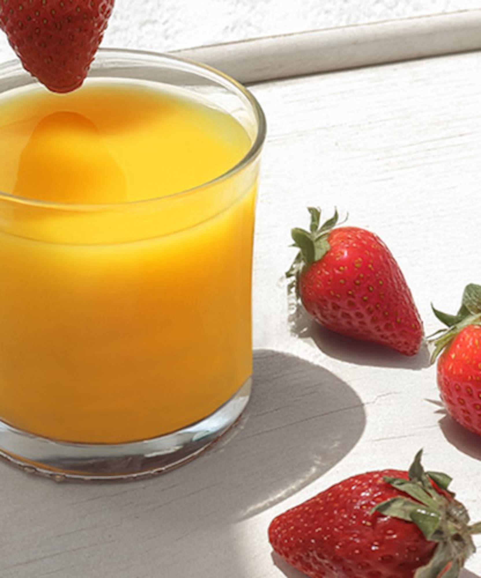Glass of orange juice, fresh strawberries, one dropping into juice.