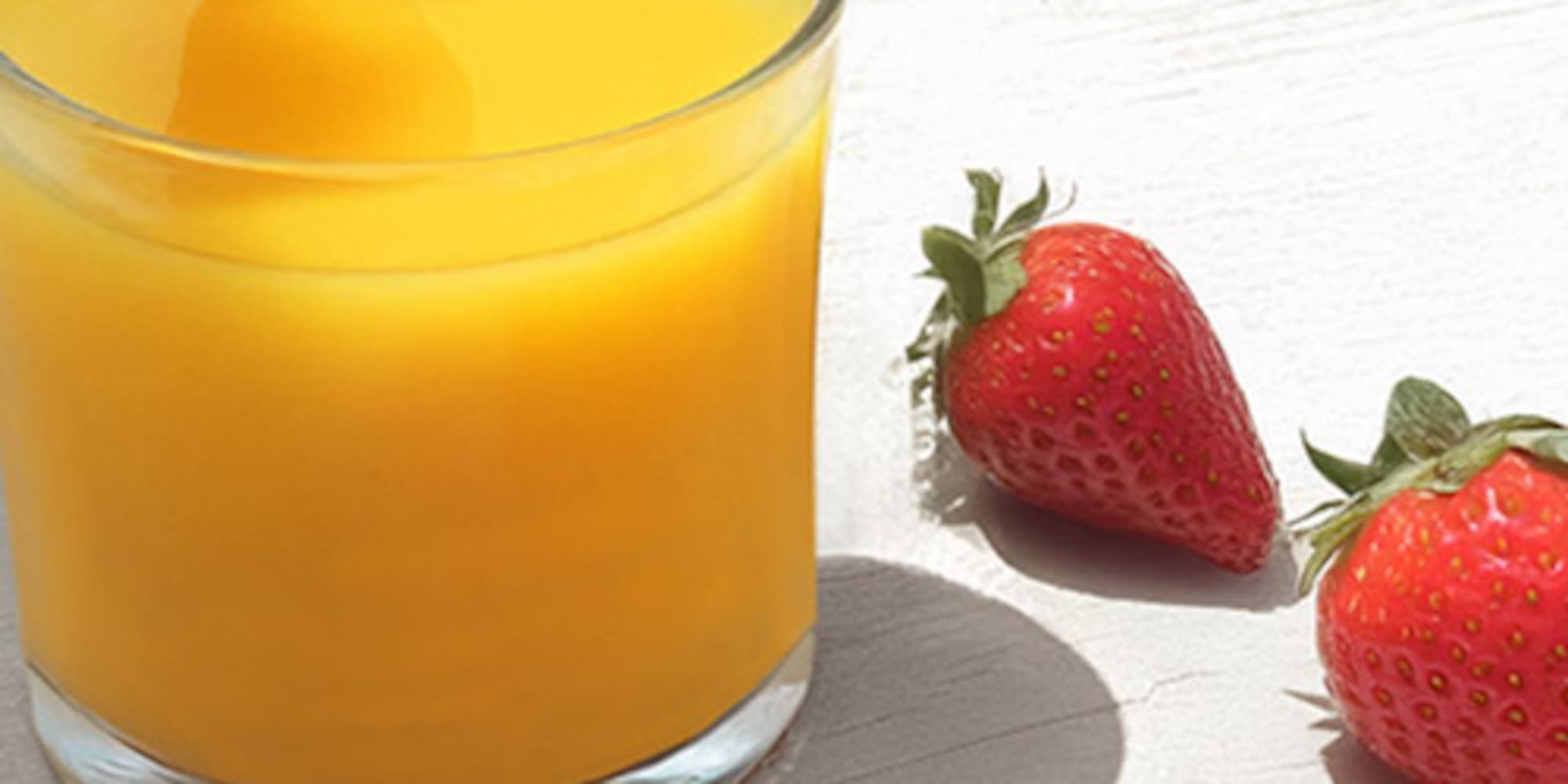 Strawberry dropping into glass of orange juice, with fresh strawberries.