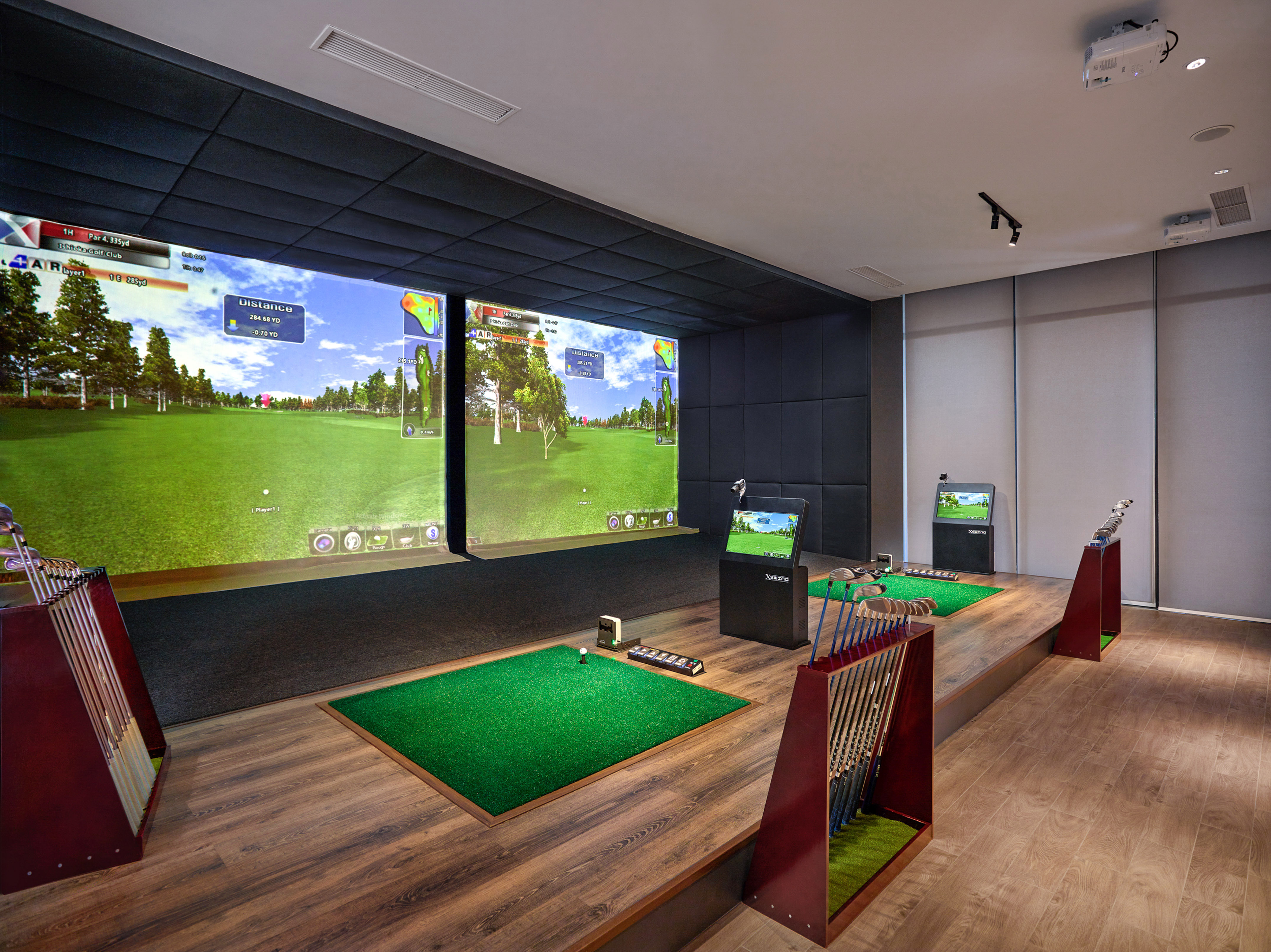 Indoor golf simulator bays with virtual course screens and golf clubs.