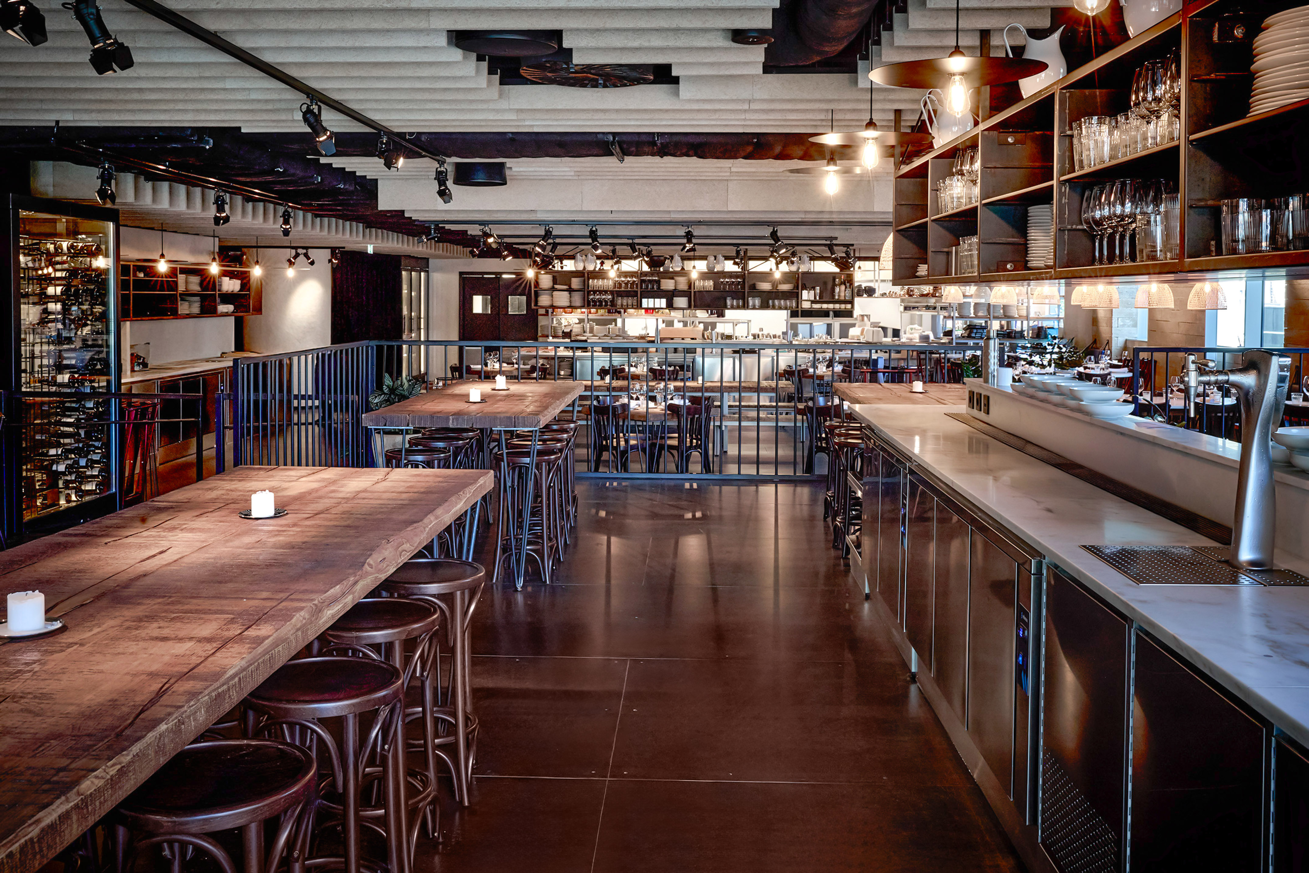 Modern restaurant bar interior with long wooden communal tables and industrial lighting.