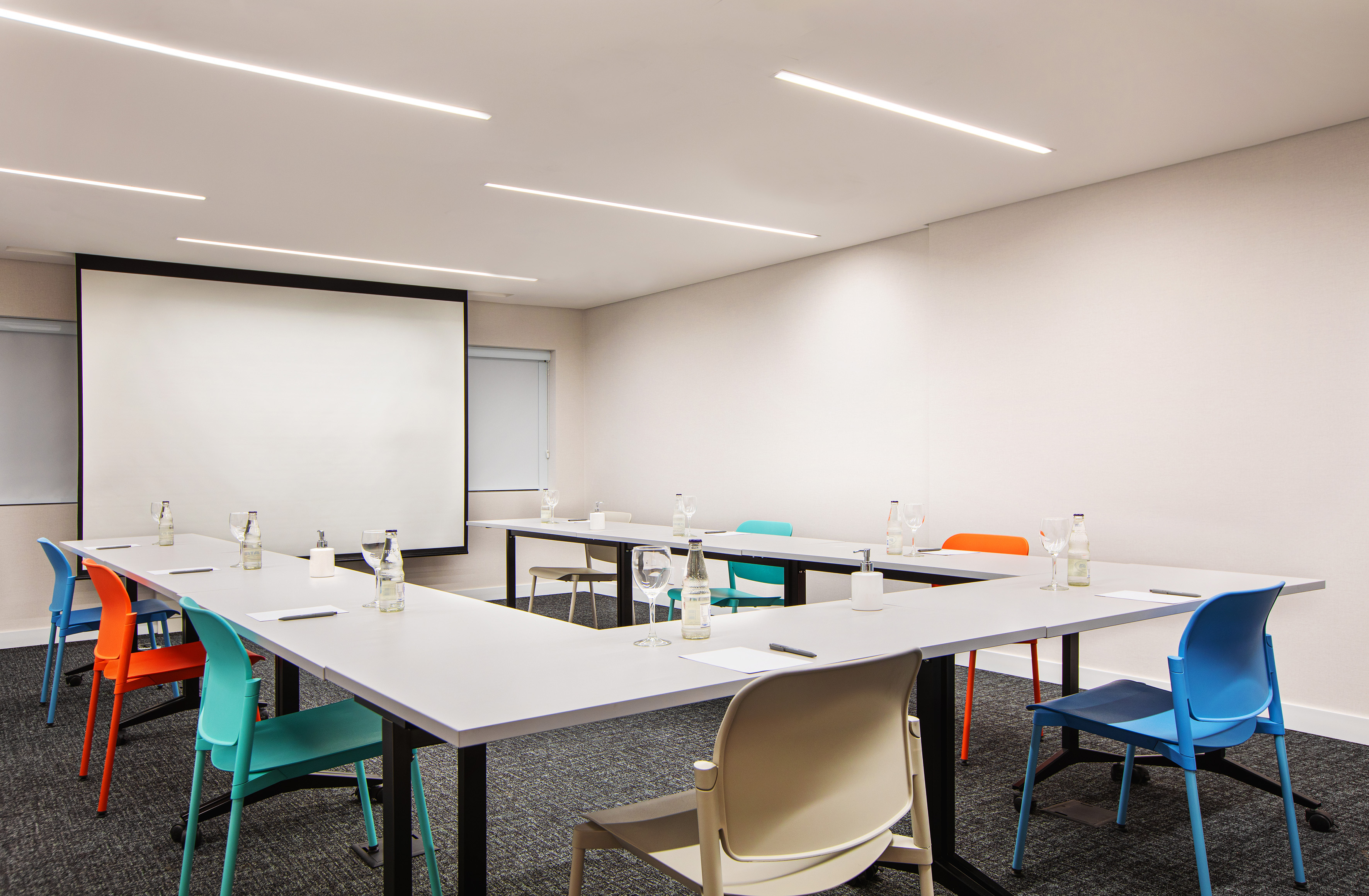 Modern U-shaped meeting room setup with projector screen and colorful chairs.