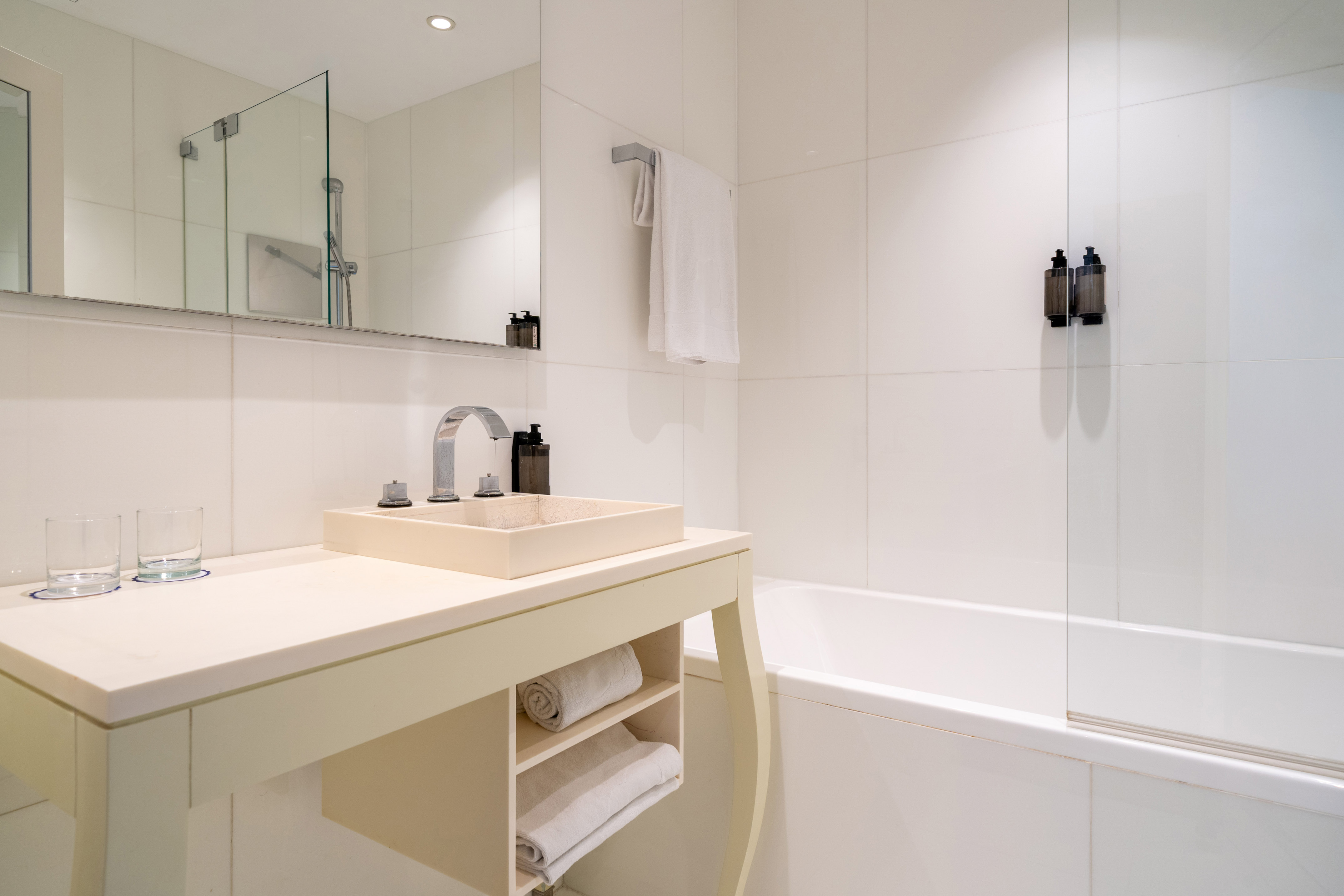 Modern white bathroom with beige vanity, sink, chrome faucet, and bathtub.