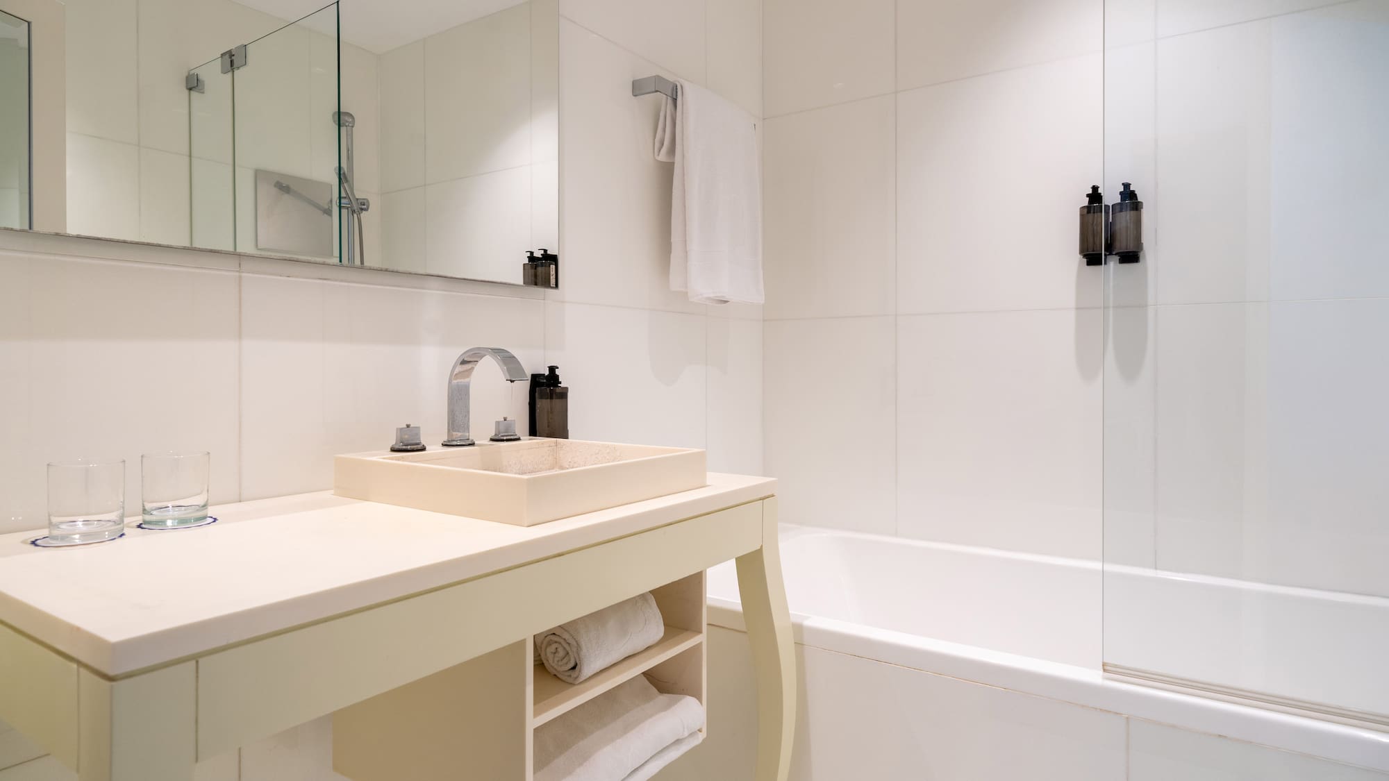 Modern white bathroom with beige vanity, sink, chrome faucet, and bathtub.