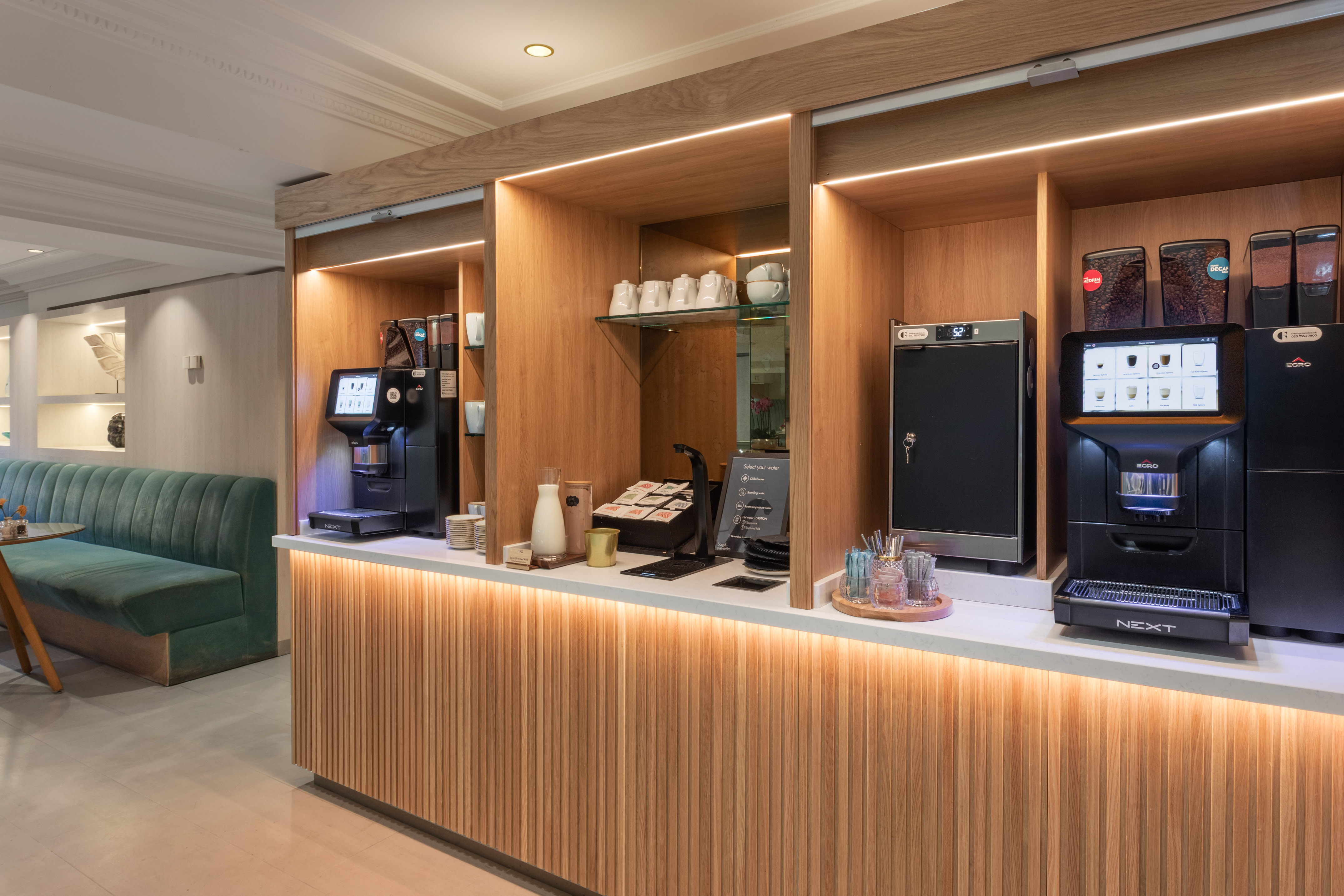 Modern self-service coffee bar with espresso machines, wooden counter, and lounge.