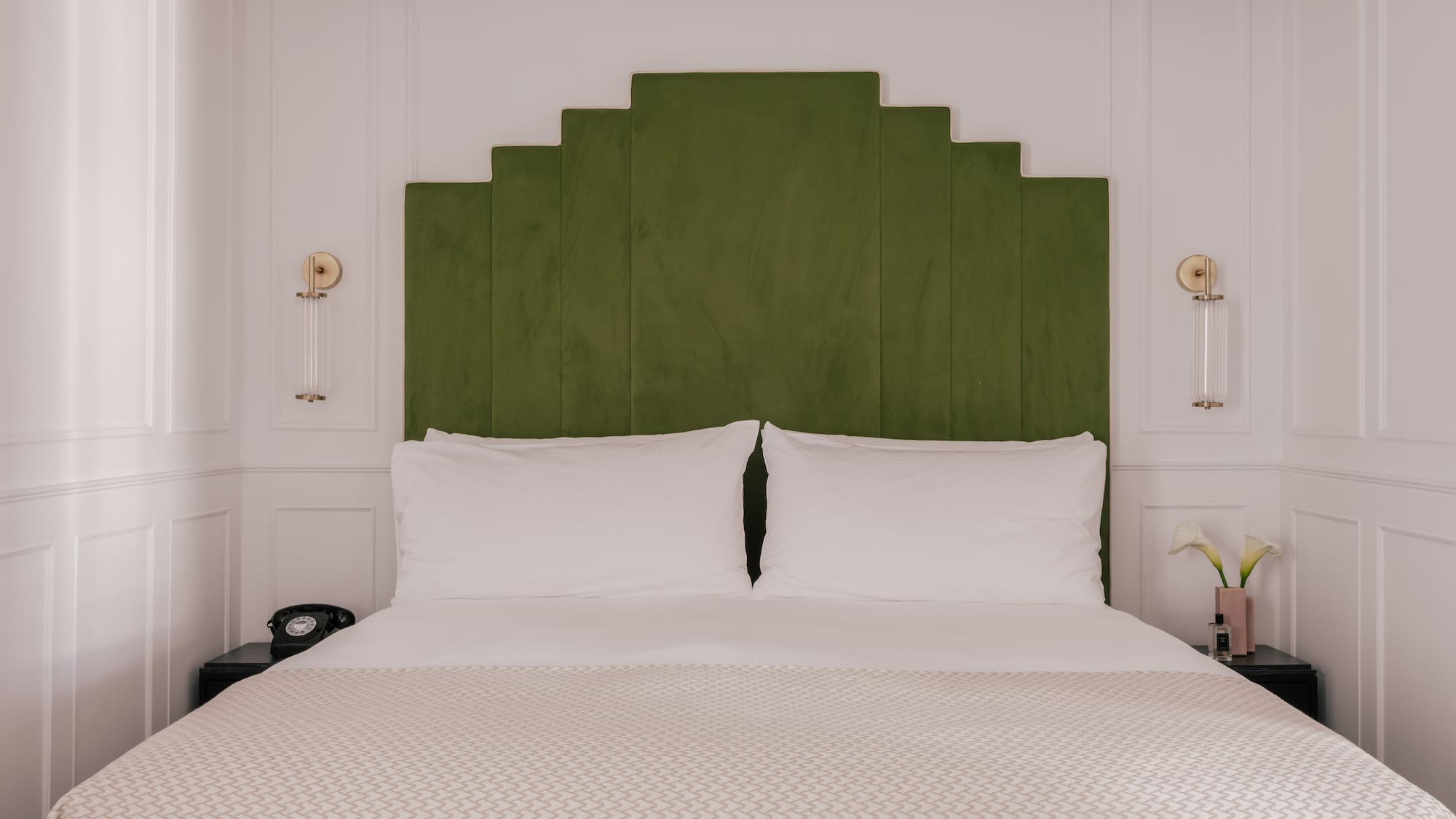 Modern bedroom with green velvet geometric headboard and white bedding.