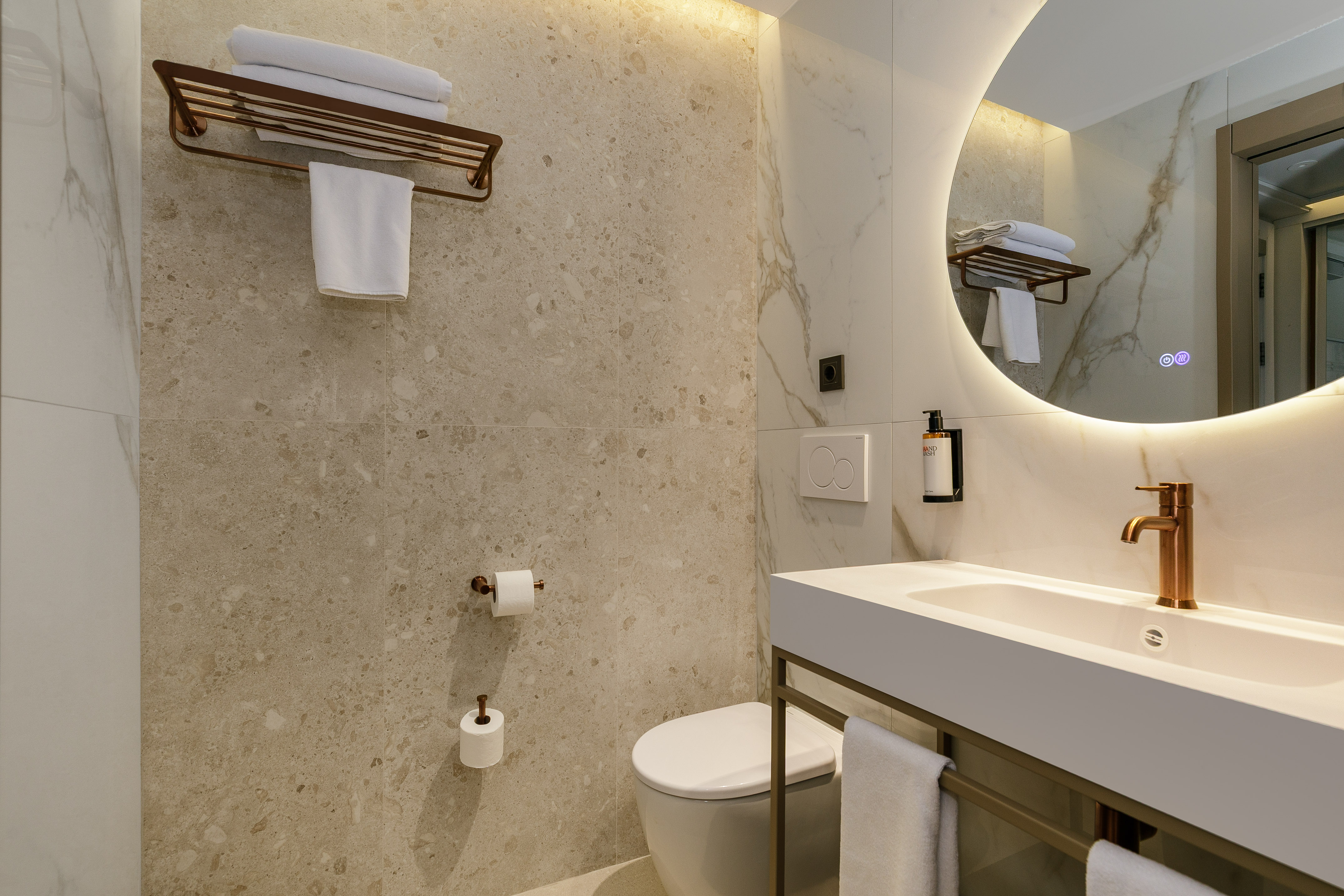 Modern bathroom with white vanity, toilet, backlit mirror, and bronze fixtures.