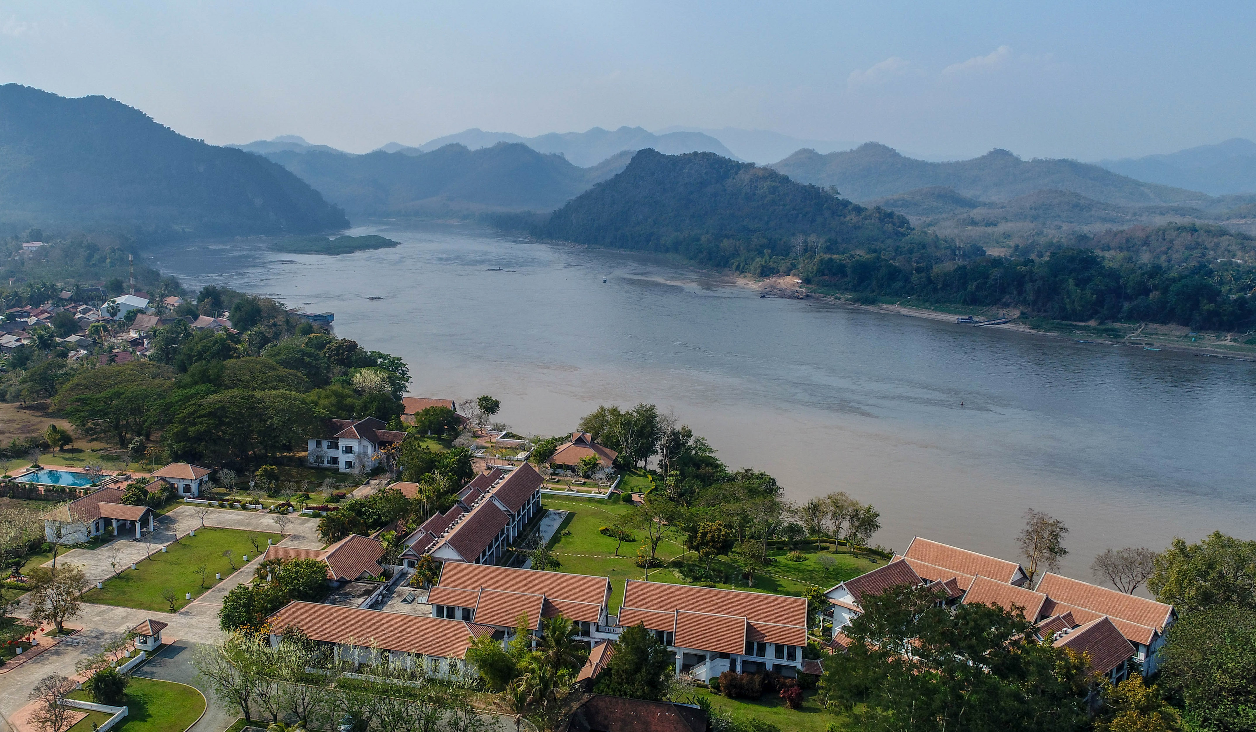 Luang Prabang riverfront resort along Mekong River, green mountains.