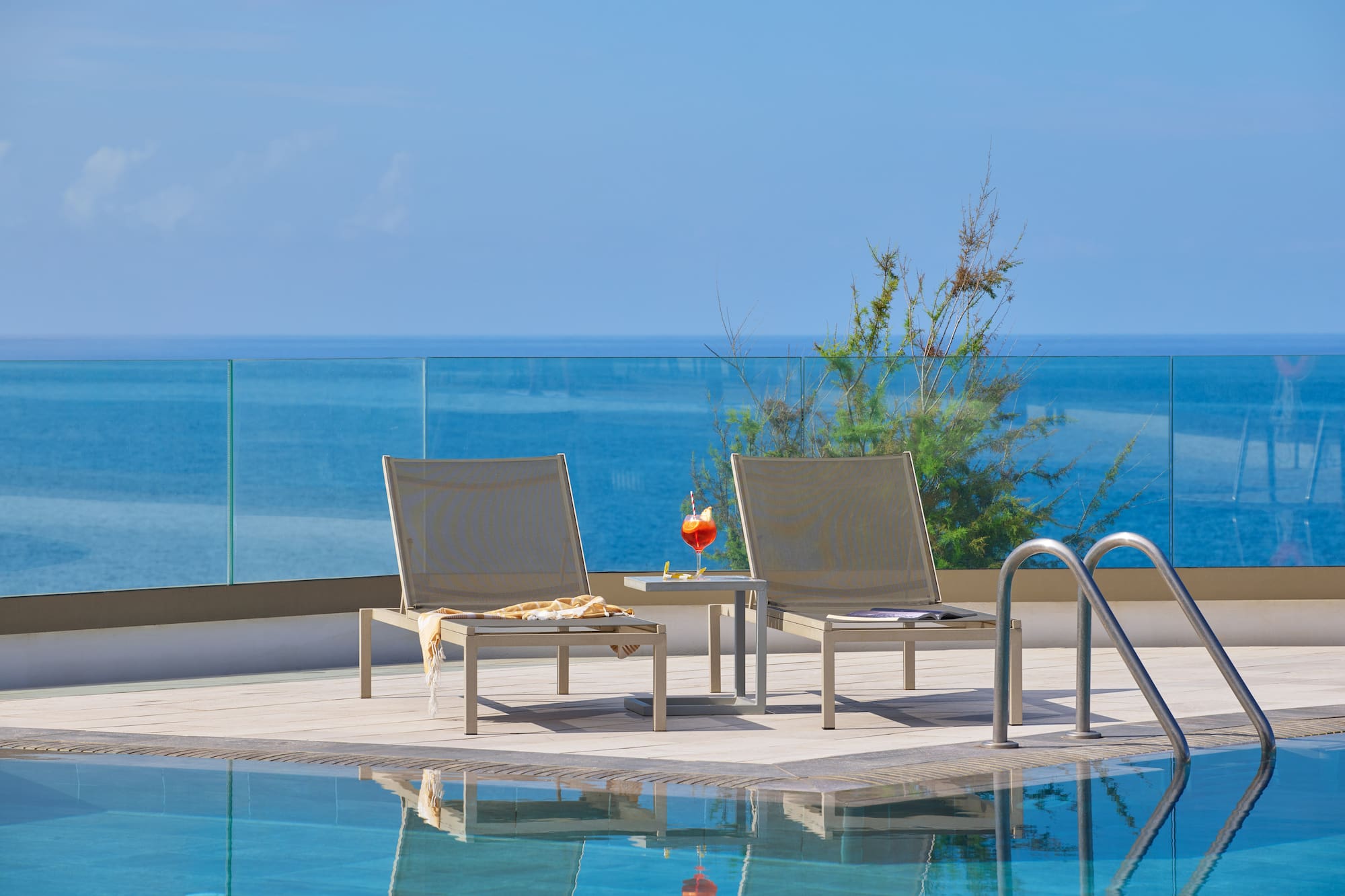 Poolside sun loungers, cocktail, and stunning ocean view from resort terrace.