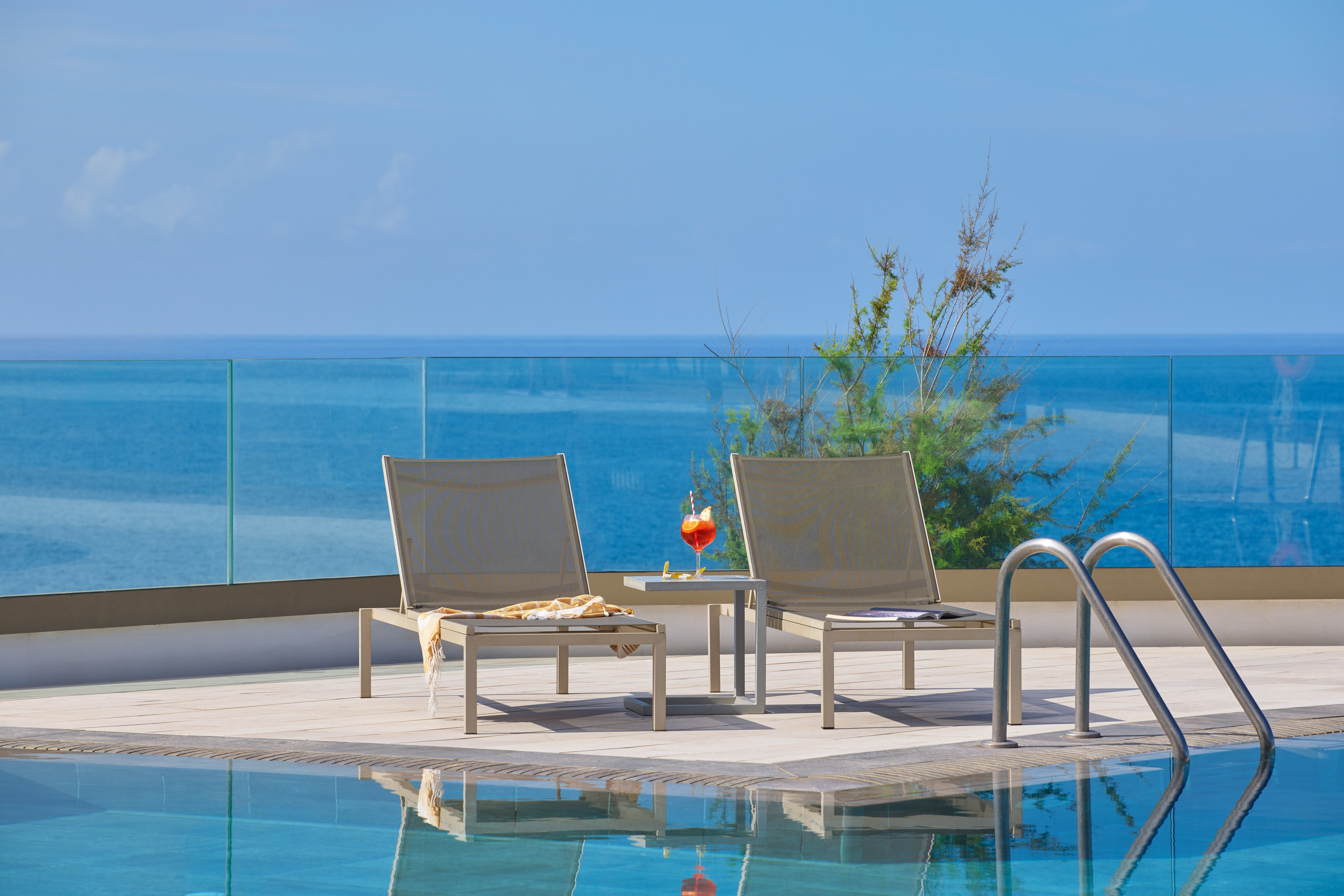 Poolside sun loungers, cocktail, and stunning ocean view from resort terrace.