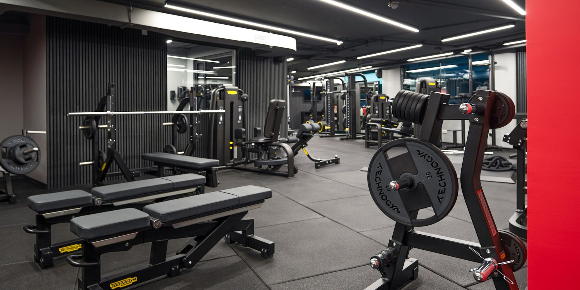 Modern gym with Technogym weightlifting equipment, exercise benches, and machines.