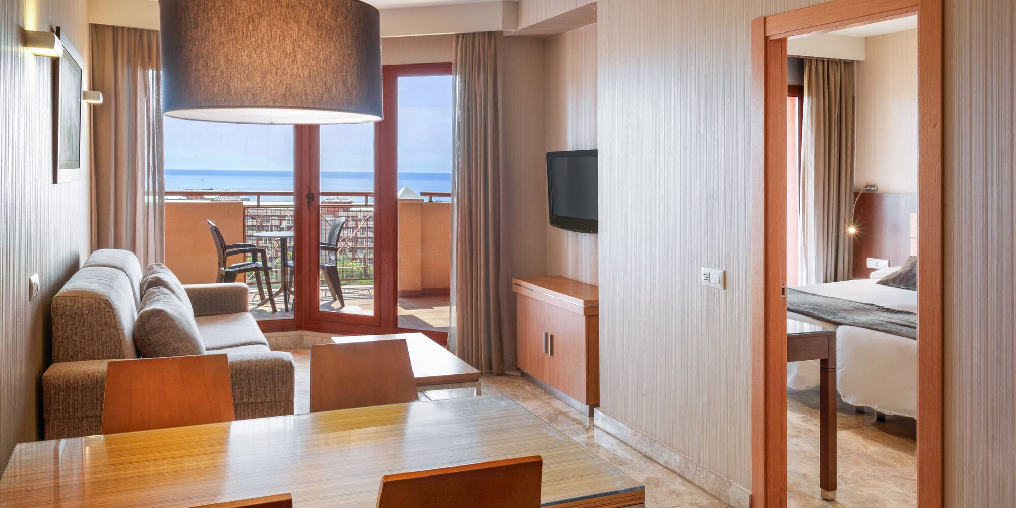 Modern hotel suite with living/dining area, sea view balcony, and bedroom.