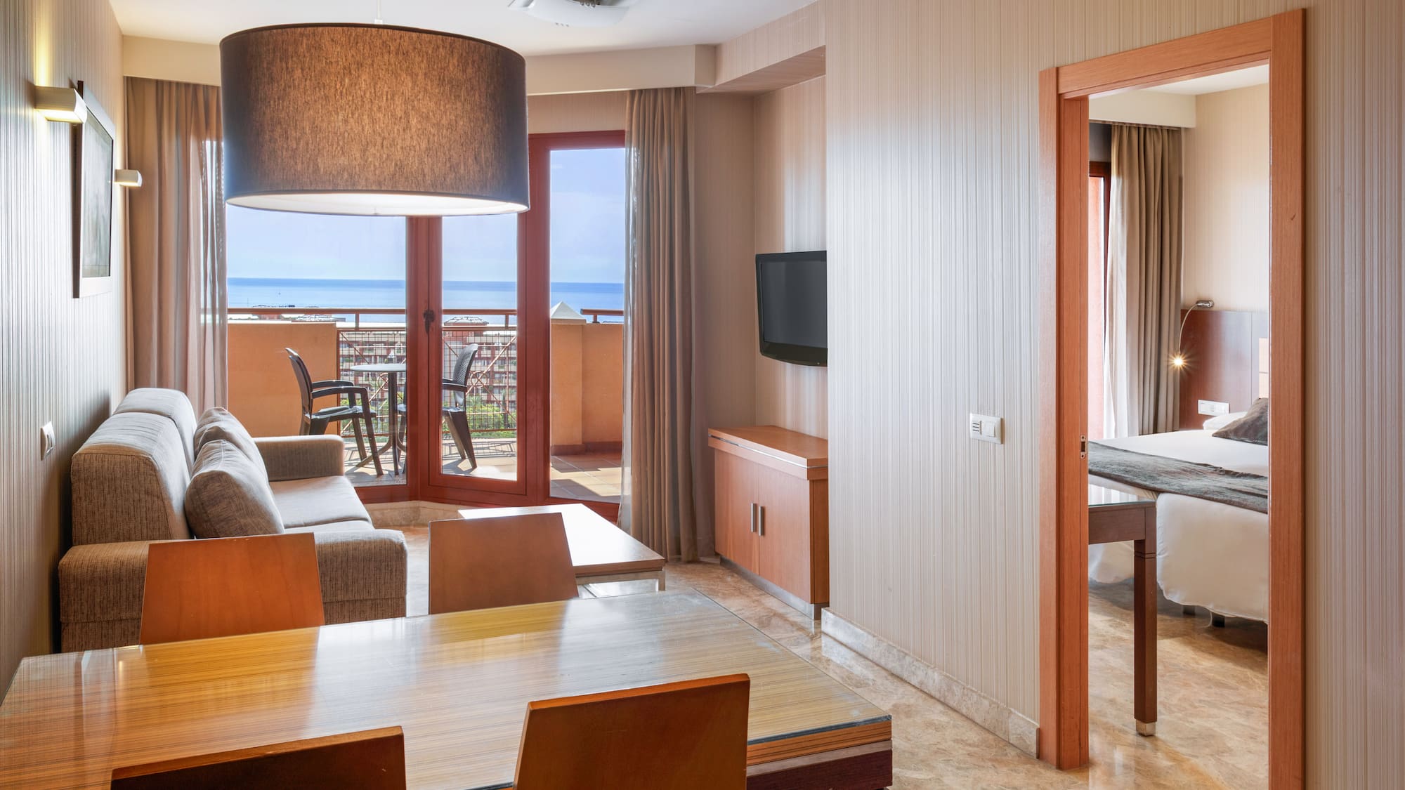 Modern hotel suite with living/dining area, sea view balcony, and bedroom.