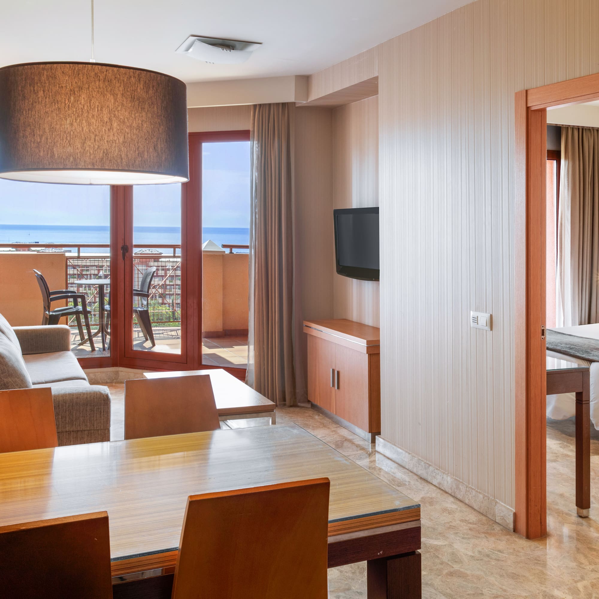 Modern hotel suite with living/dining area, sea view balcony, and bedroom.