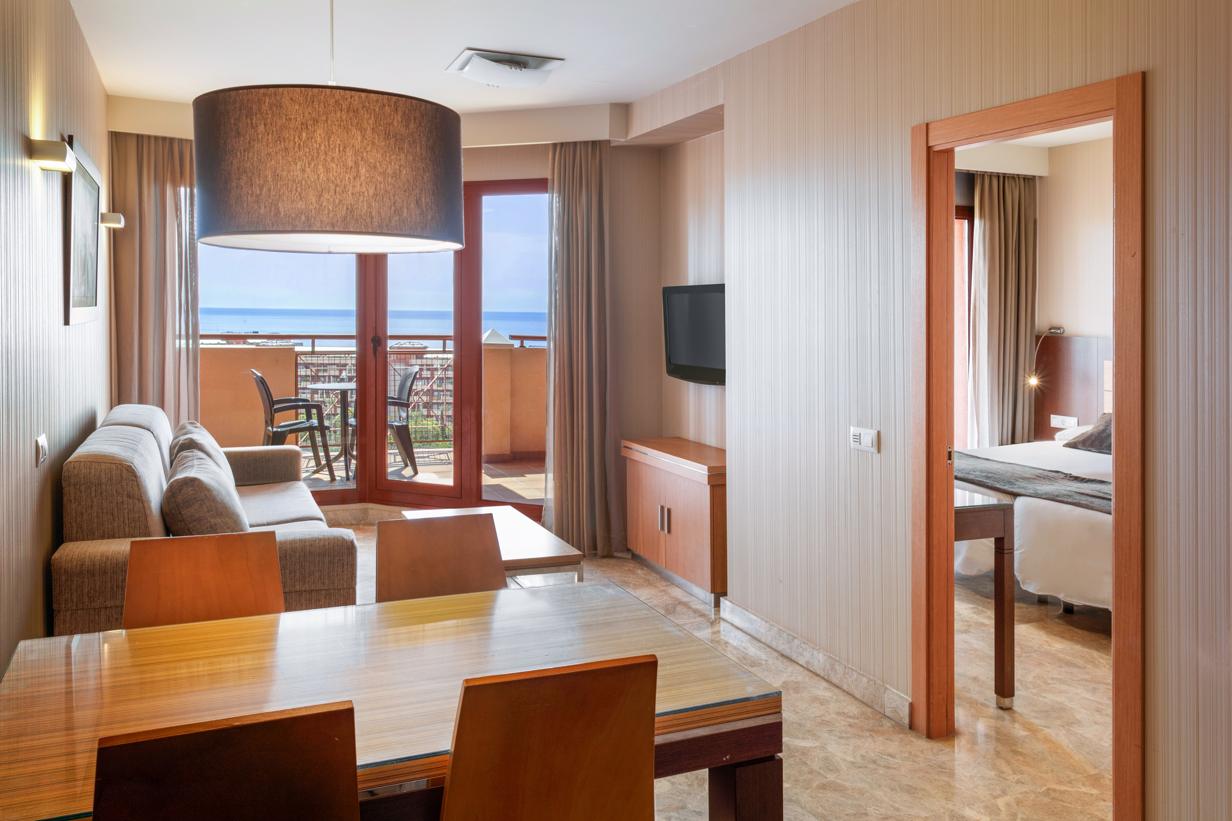 Hotel suite living & dining room with sea view balcony and bedroom access.