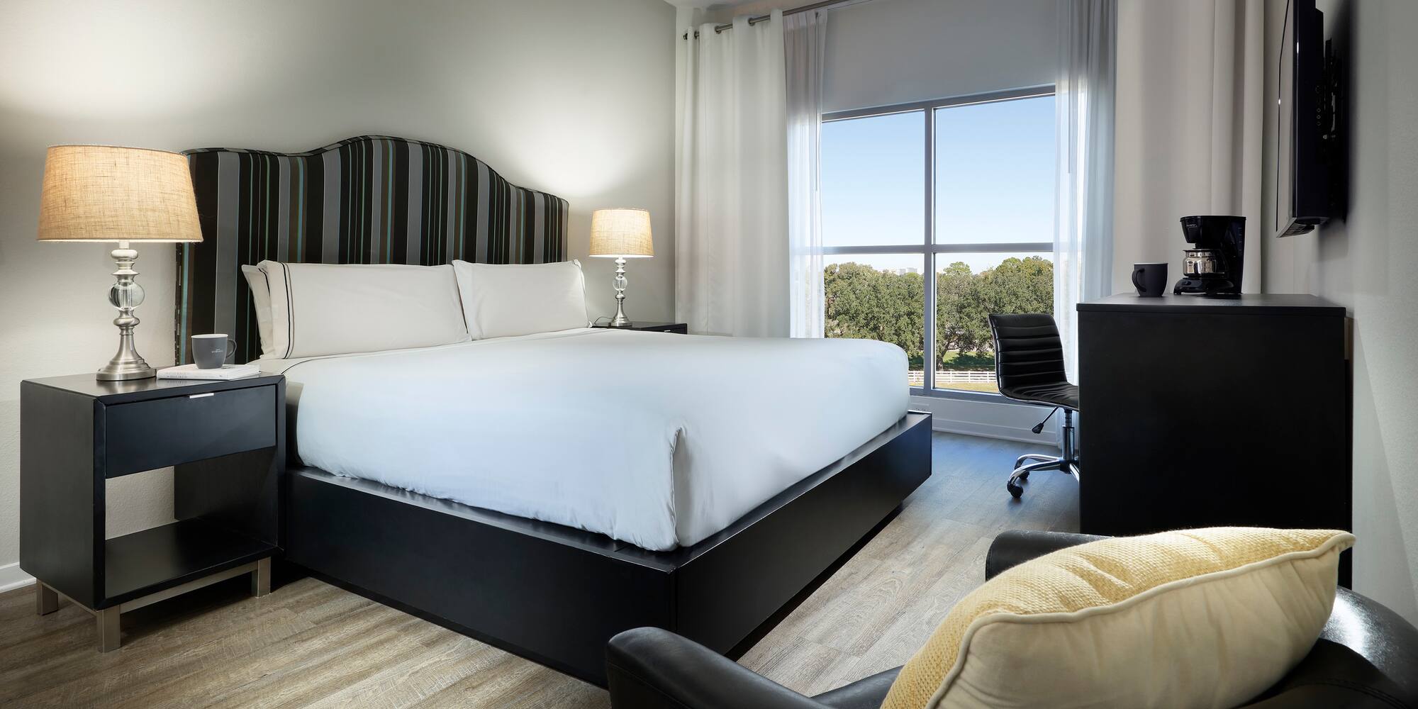 Modern hotel room with king bed, striped headboard, work desk, and scenic window.
