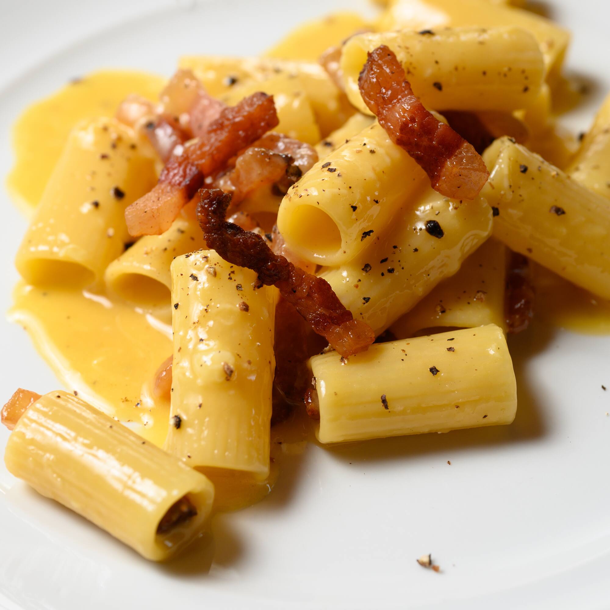 a plate of pasta with bacon and sauce