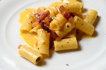 a plate of pasta with bacon and sauce