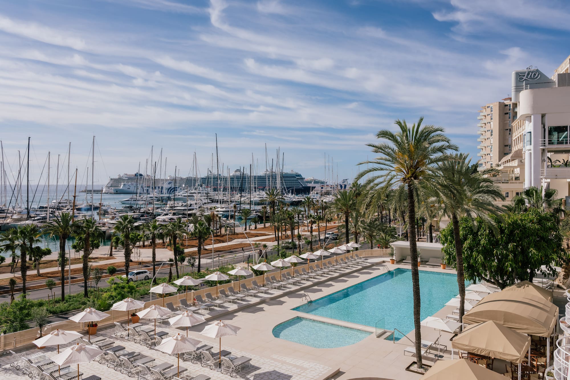 Piscina de hotel con tumbonas, palmeras y puerto deportivo con yates y cruceros.