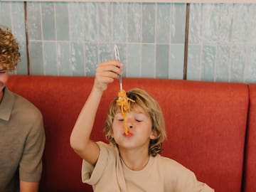 a boy holding a fork over his face while eating spaghetti