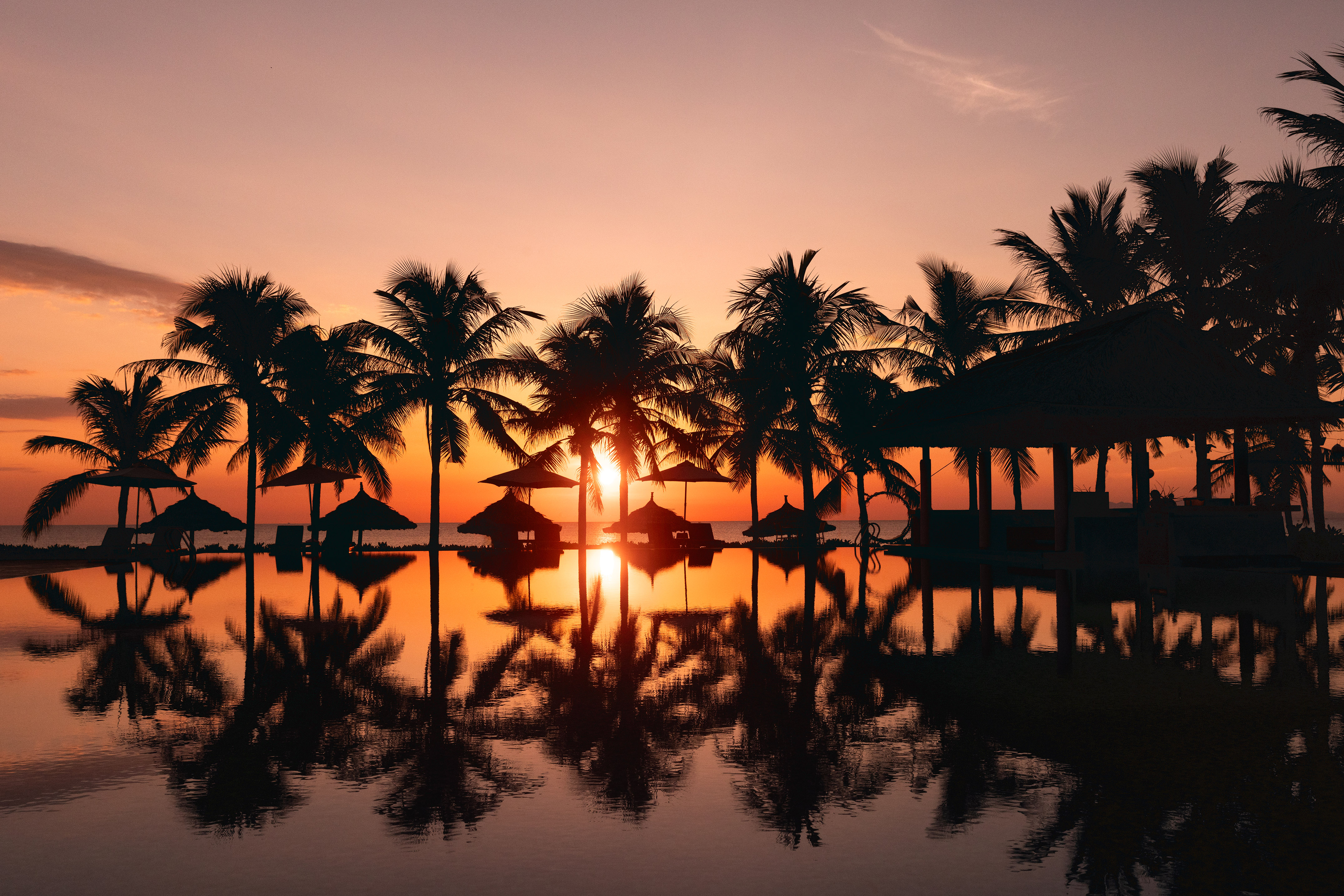 a sunset over a body of water with palm trees