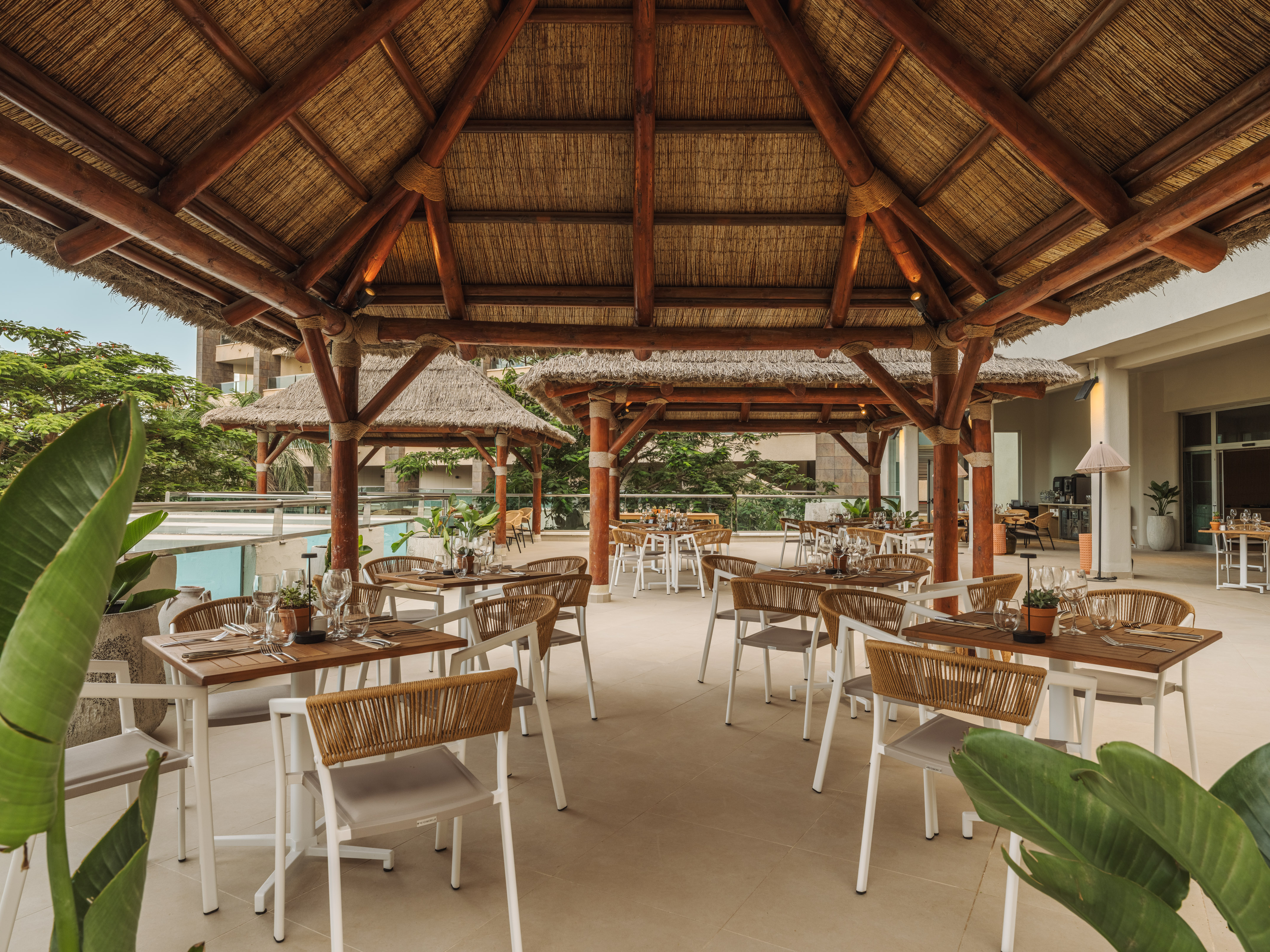 Tropical outdoor dining patio under a large thatched roof.
