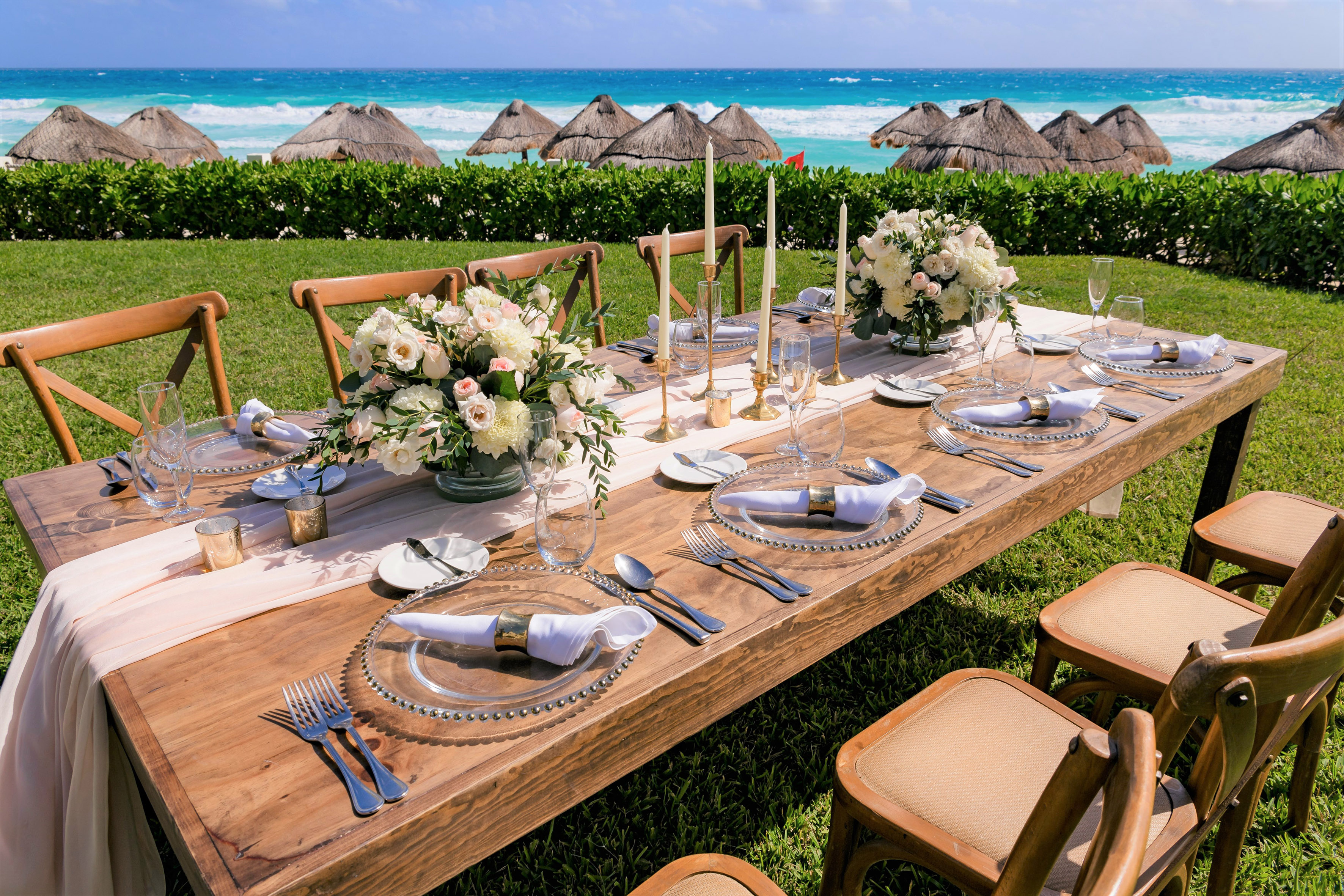 Oceanfront dining table with elegant floral decor and thatched umbrellas.
