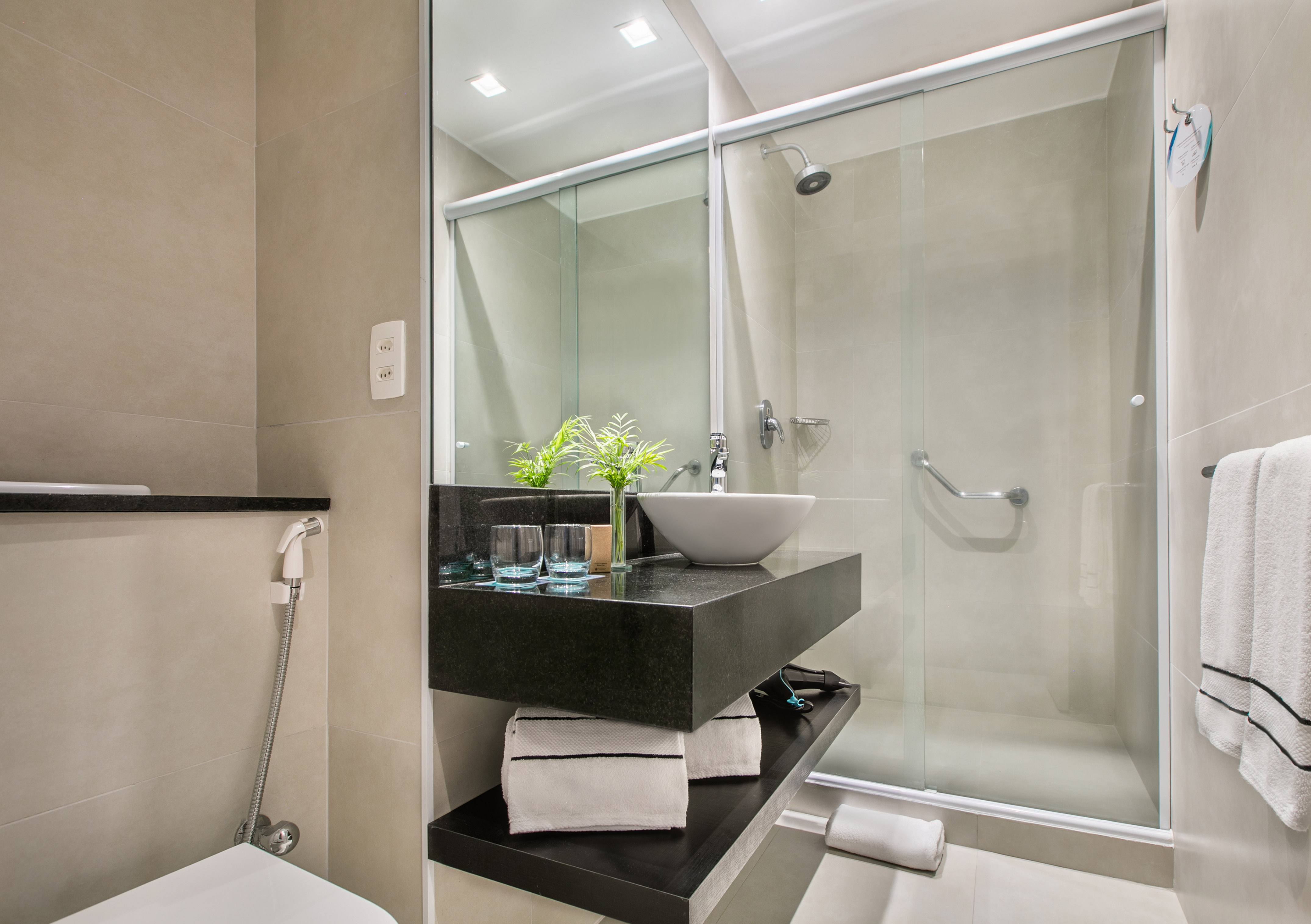 Modern bathroom with beige tiles, vessel sink, black vanity, and glass shower.