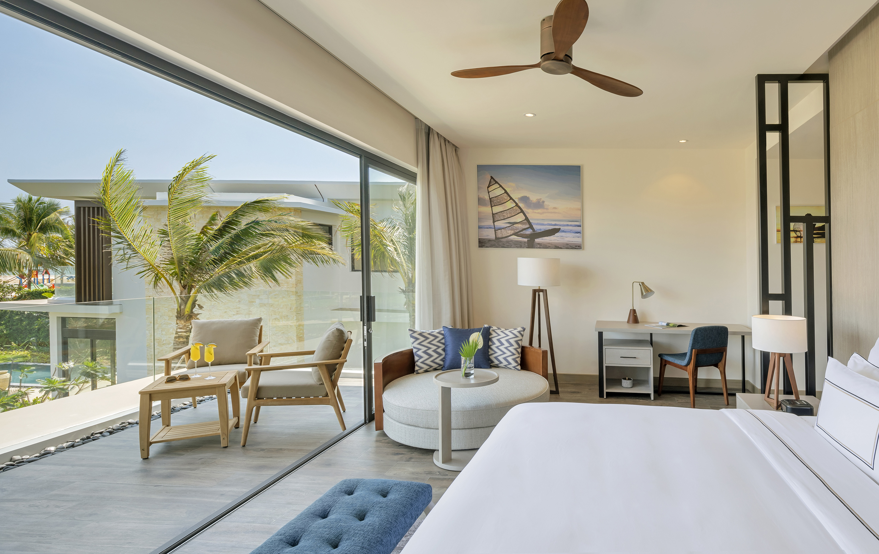 Tropical hotel room with balcony, outdoor seating, palm trees, and modern design.