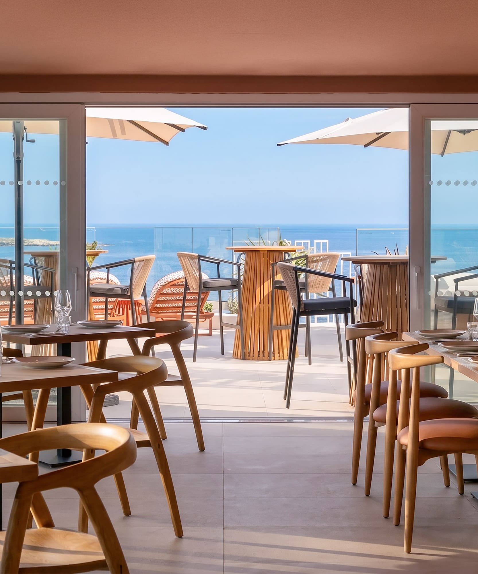 Modern restaurant interior with set tables and a bright sea view terrace.
