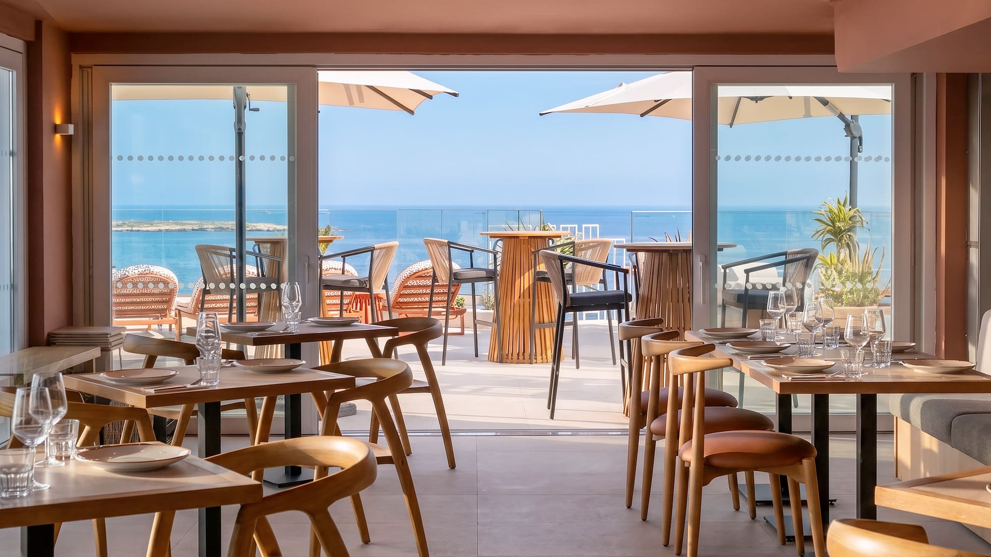 Restaurant dining area with wooden tables, chairs, and ocean view patio.