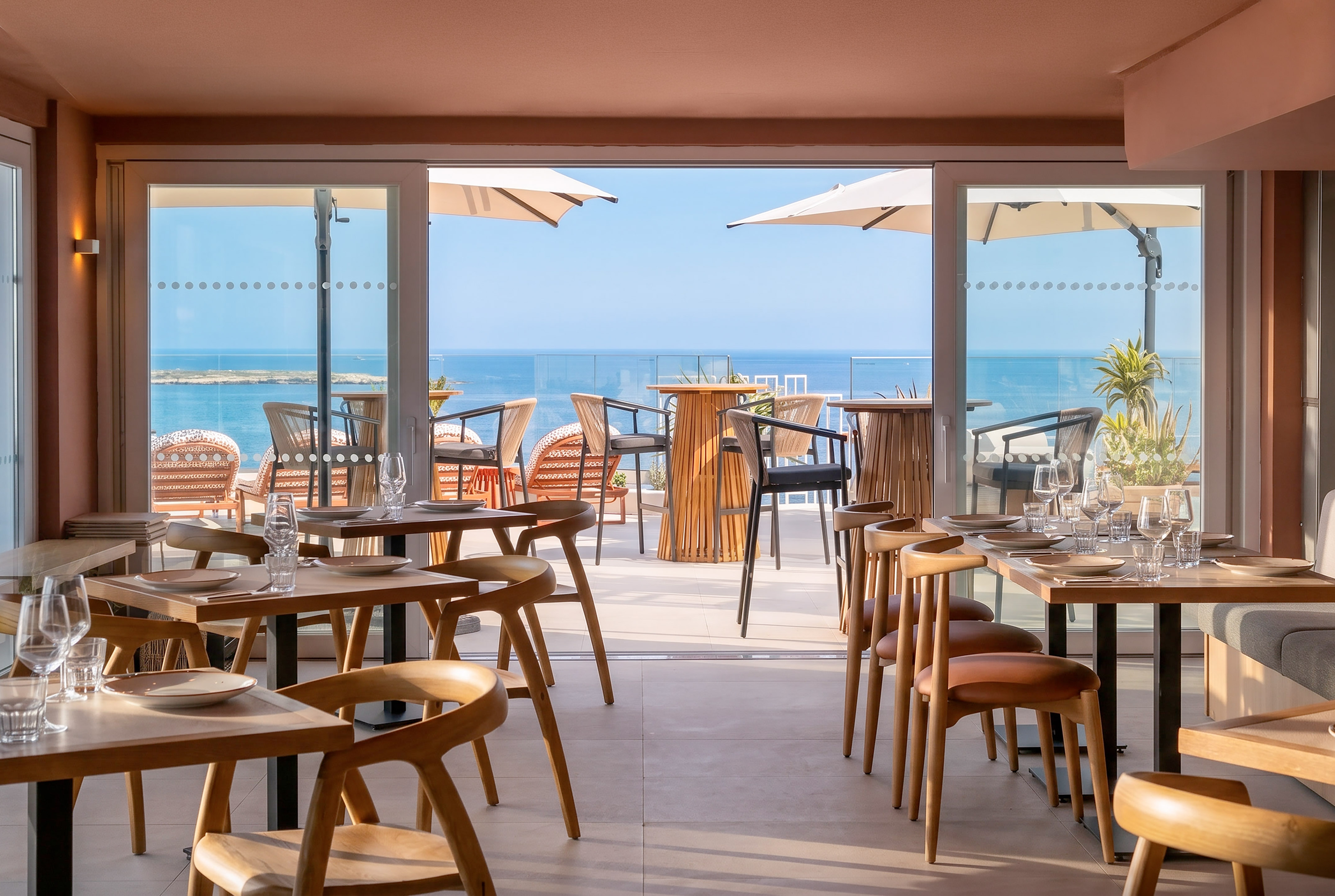 Modern restaurant interior with set tables and a bright sea view terrace.