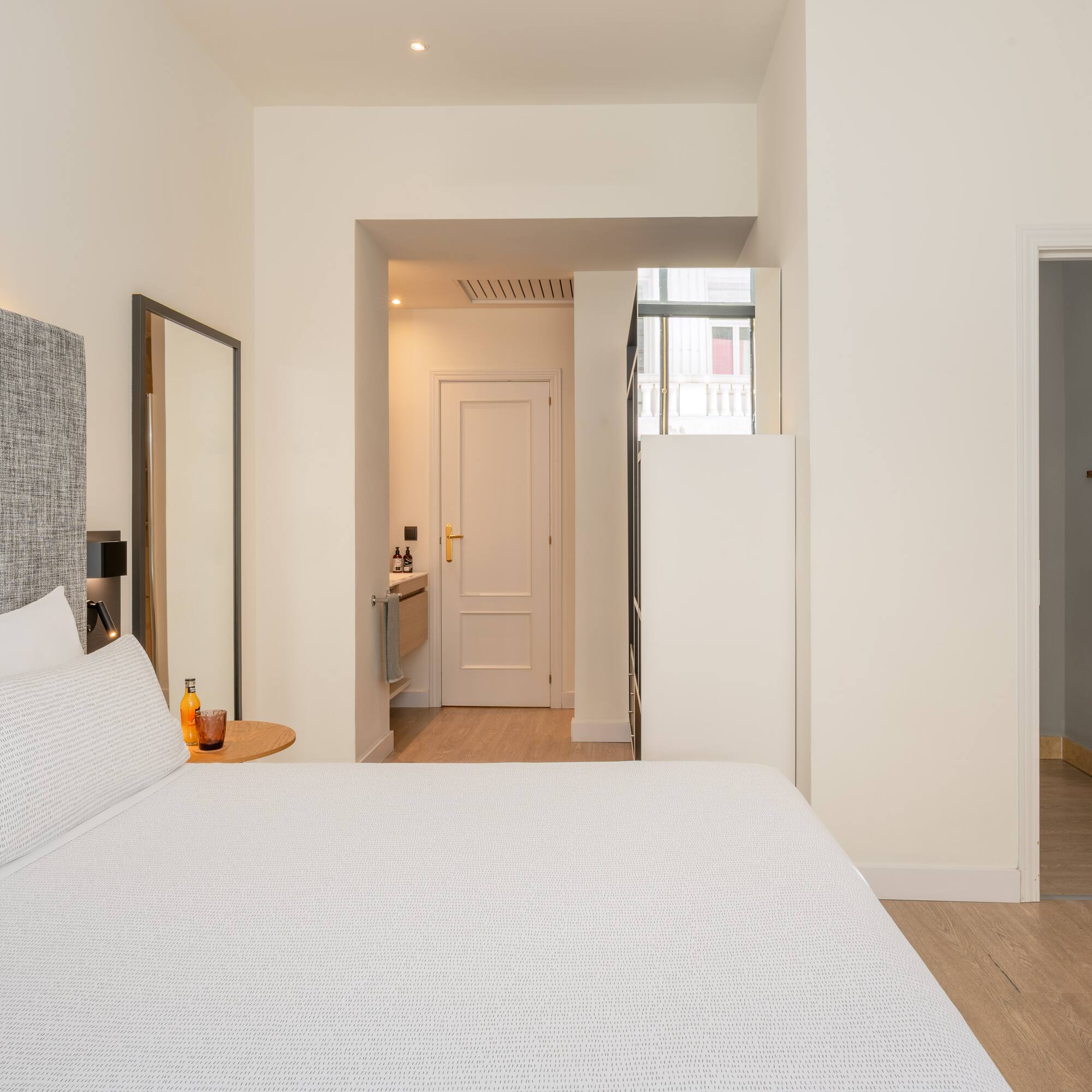 Modern hotel bedroom with white bed, grey headboard, and light wood floor.