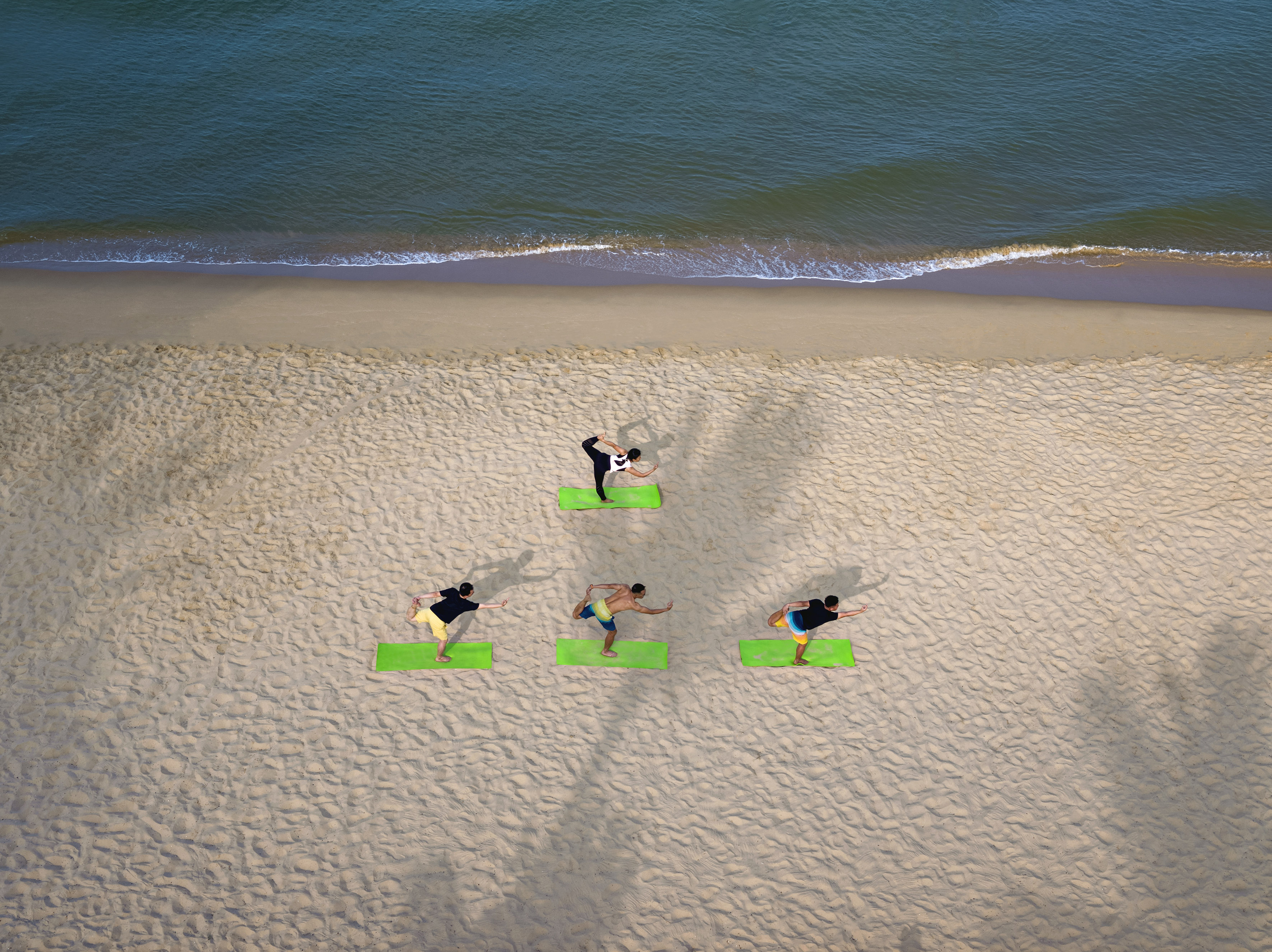 Aerial view of group beach yoga on green mats by the ocean.