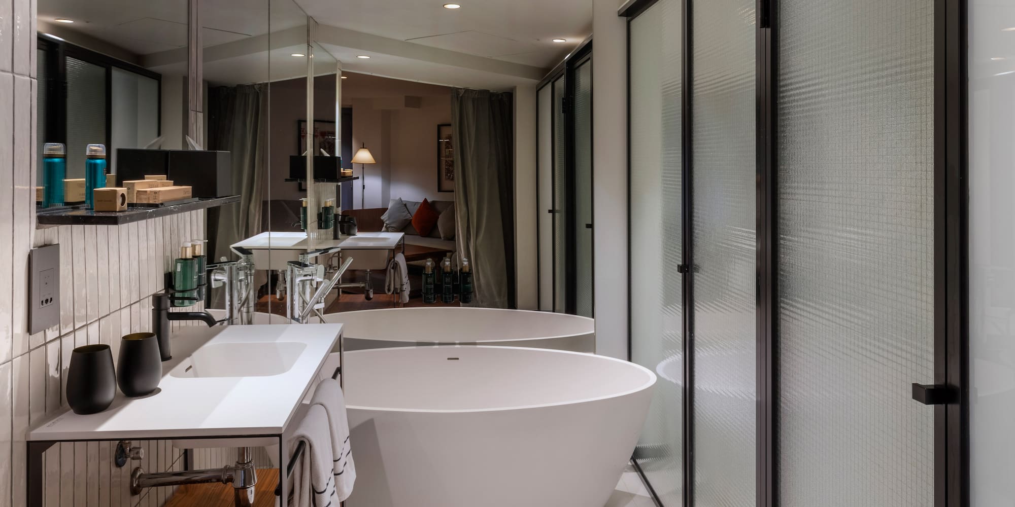 Modern hotel bathroom with freestanding tub, white vanity, and frosted glass shower.