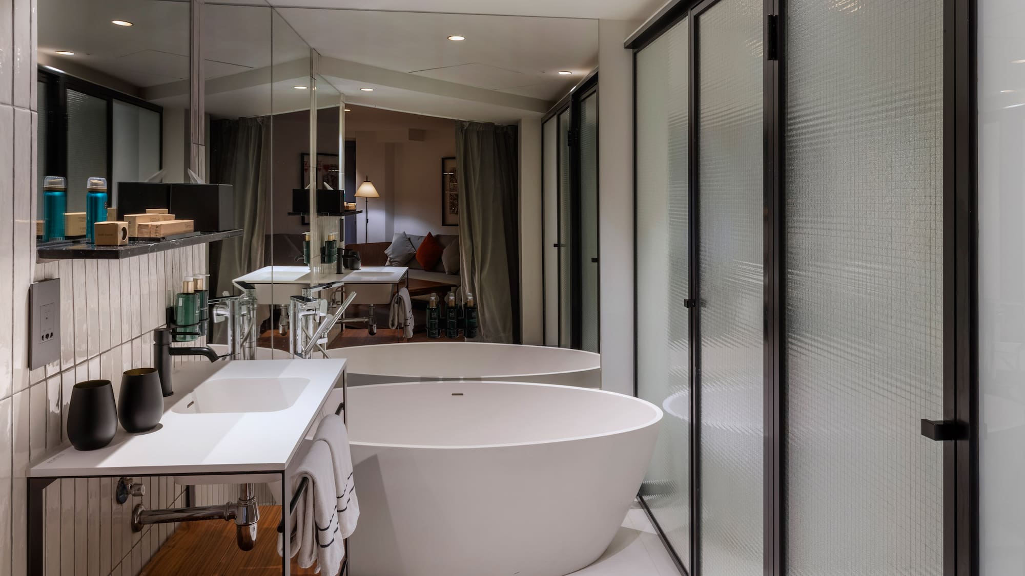 Modern hotel bathroom with freestanding tub, white vanity, and frosted glass shower.
