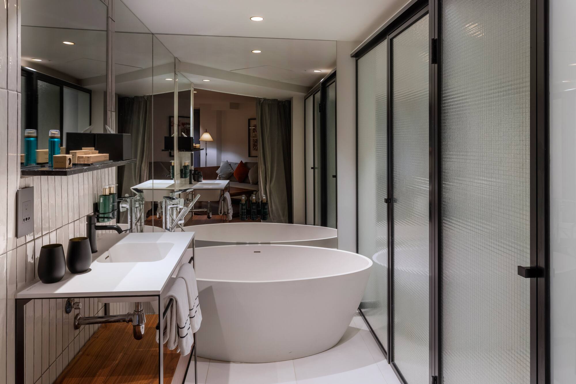 Modern hotel bathroom with freestanding tub, white vanity, and frosted glass shower.