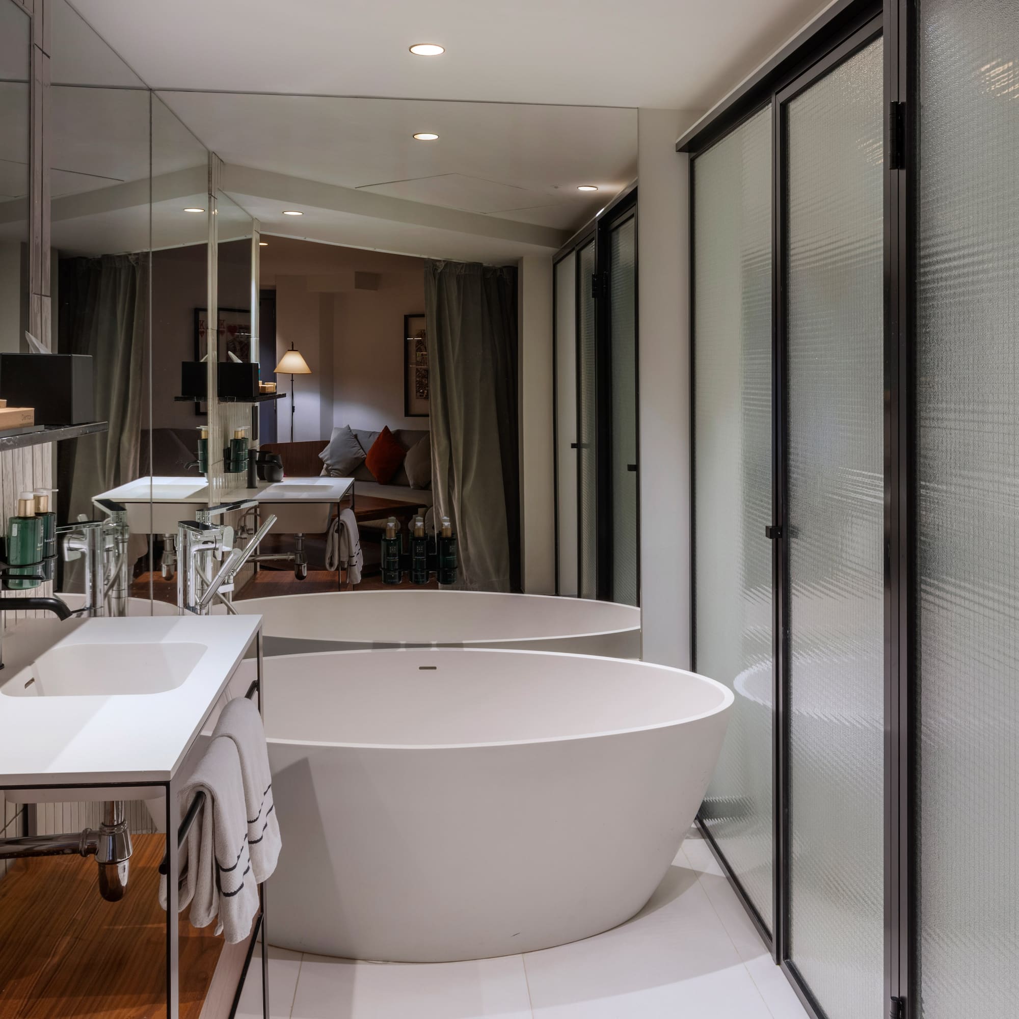 Modern hotel bathroom with freestanding tub, white vanity, and frosted glass shower.