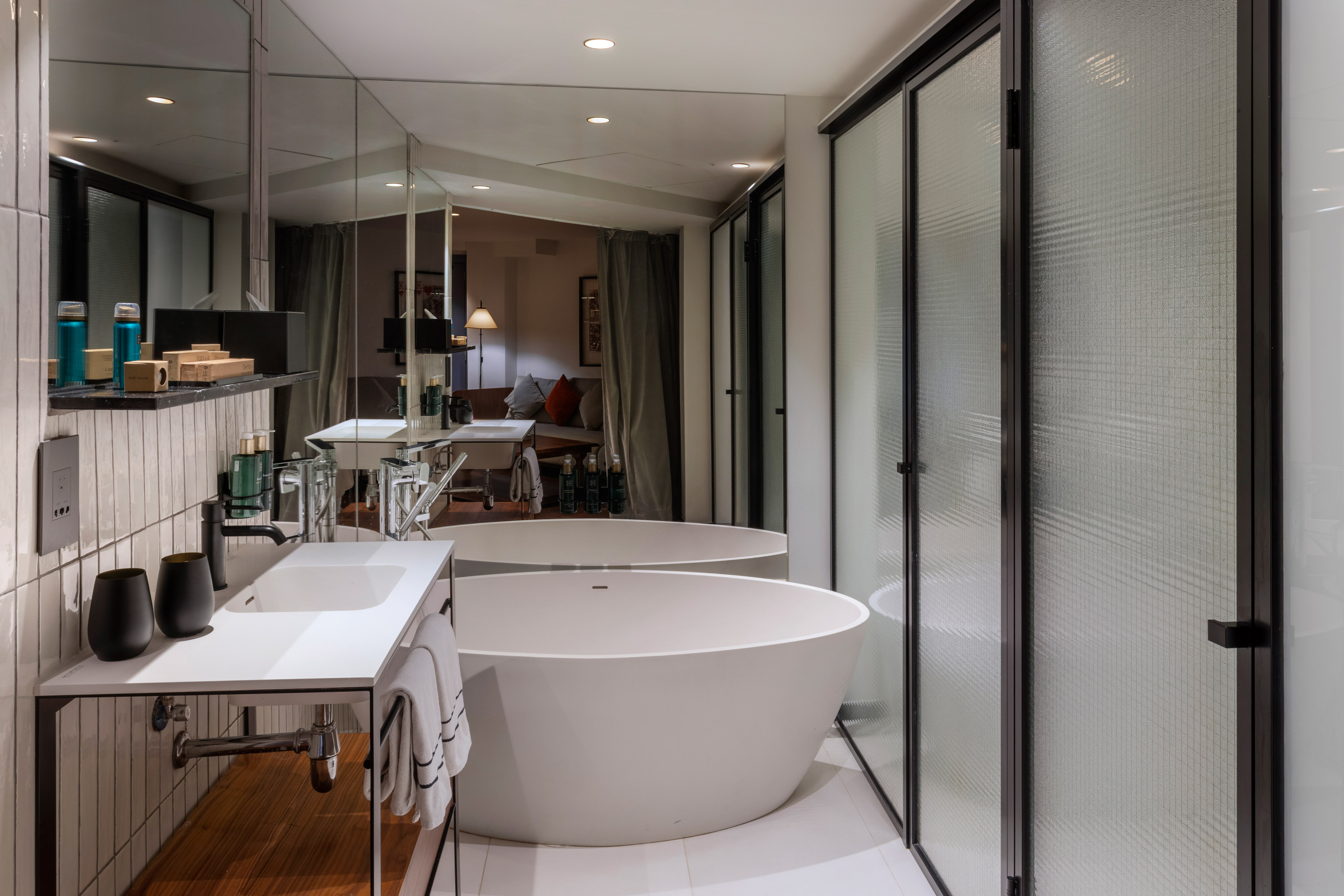 Modern hotel bathroom with freestanding tub, white vanity, and frosted glass shower.