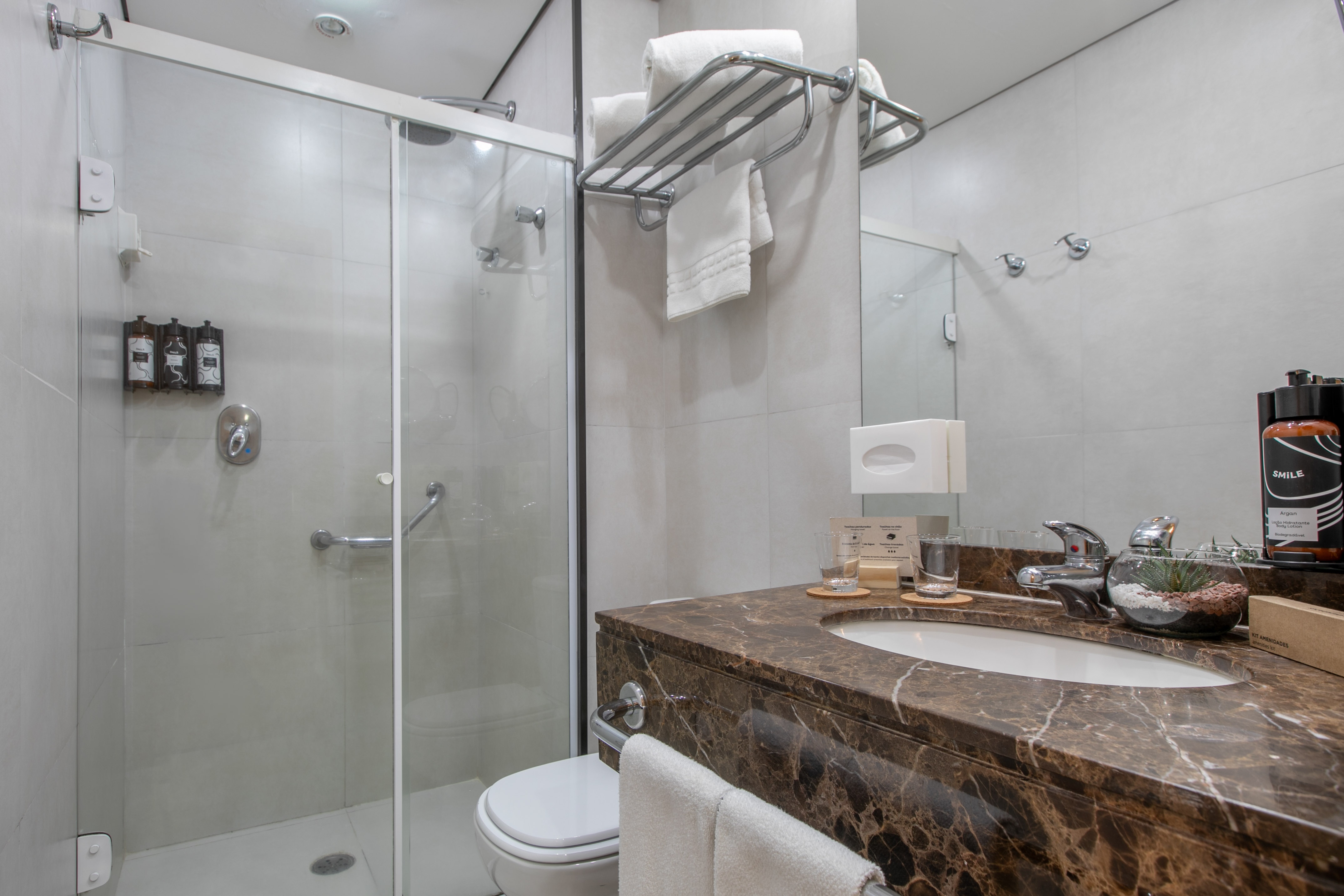 Modern hotel bathroom with glass shower, marble vanity, sink, and white towels.