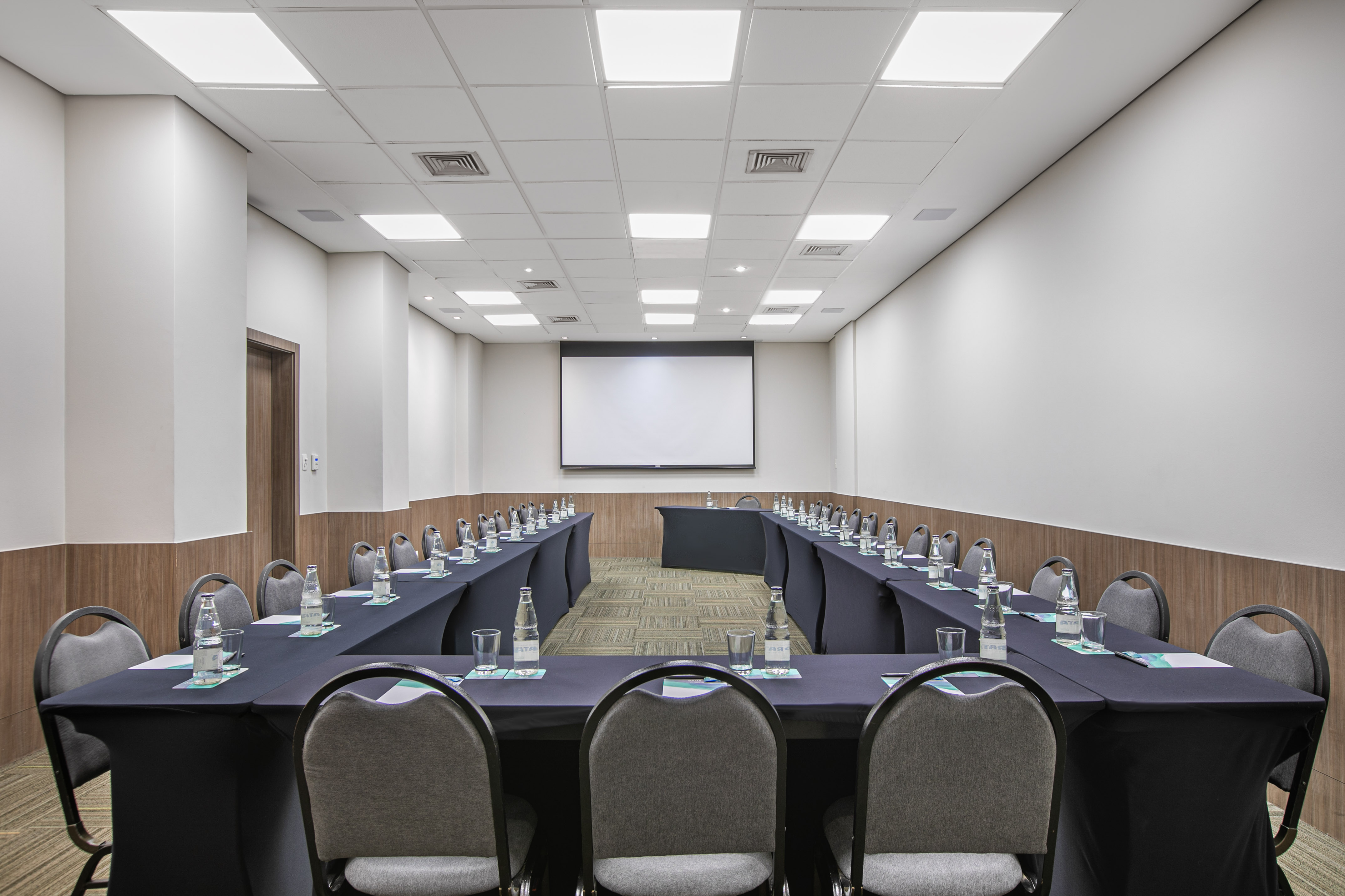 Modern U-shaped conference room with projection screen, dark tables, and chairs for meetings.