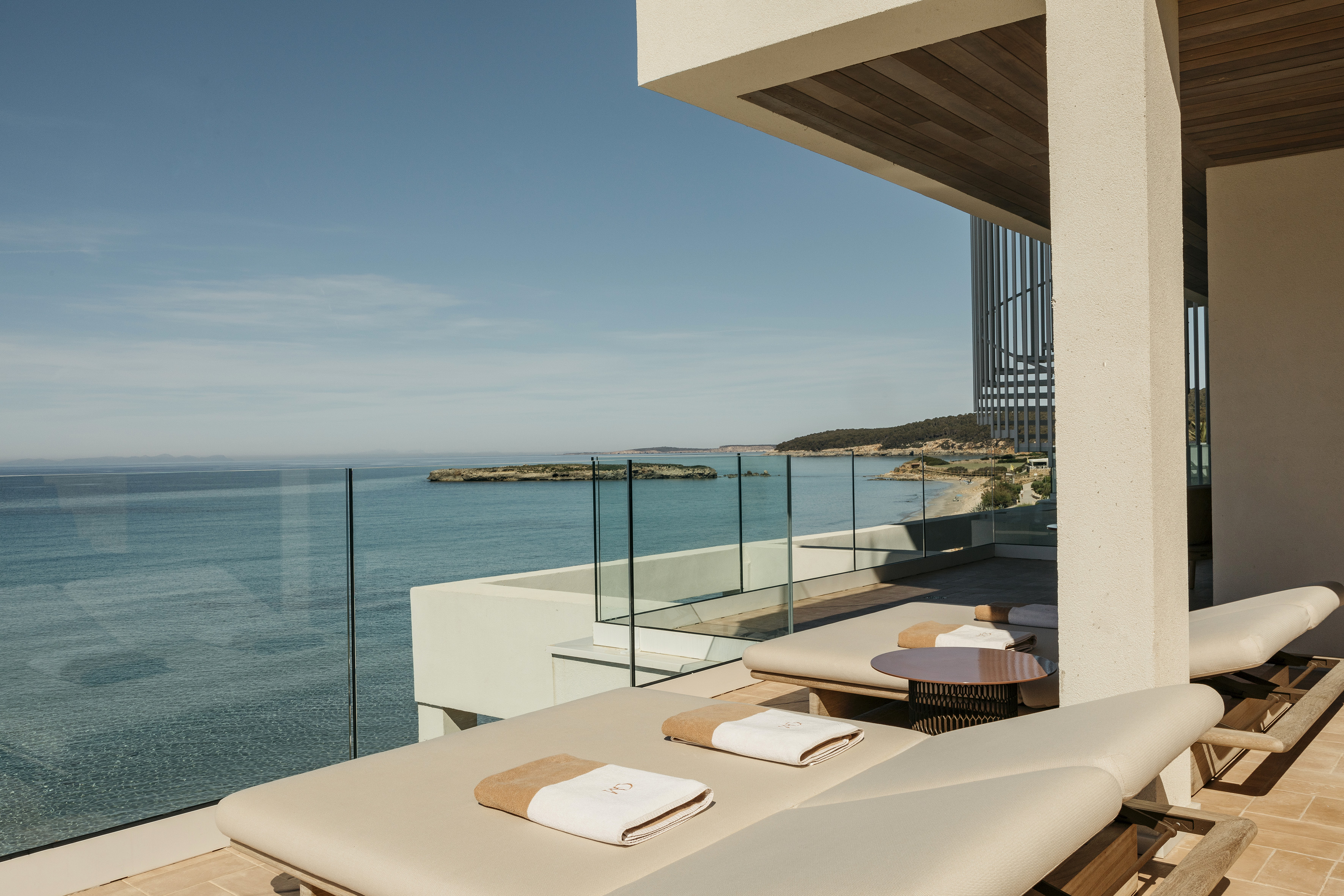 Luxury resort balcony with ocean view, lounge chairs, and distant beach.